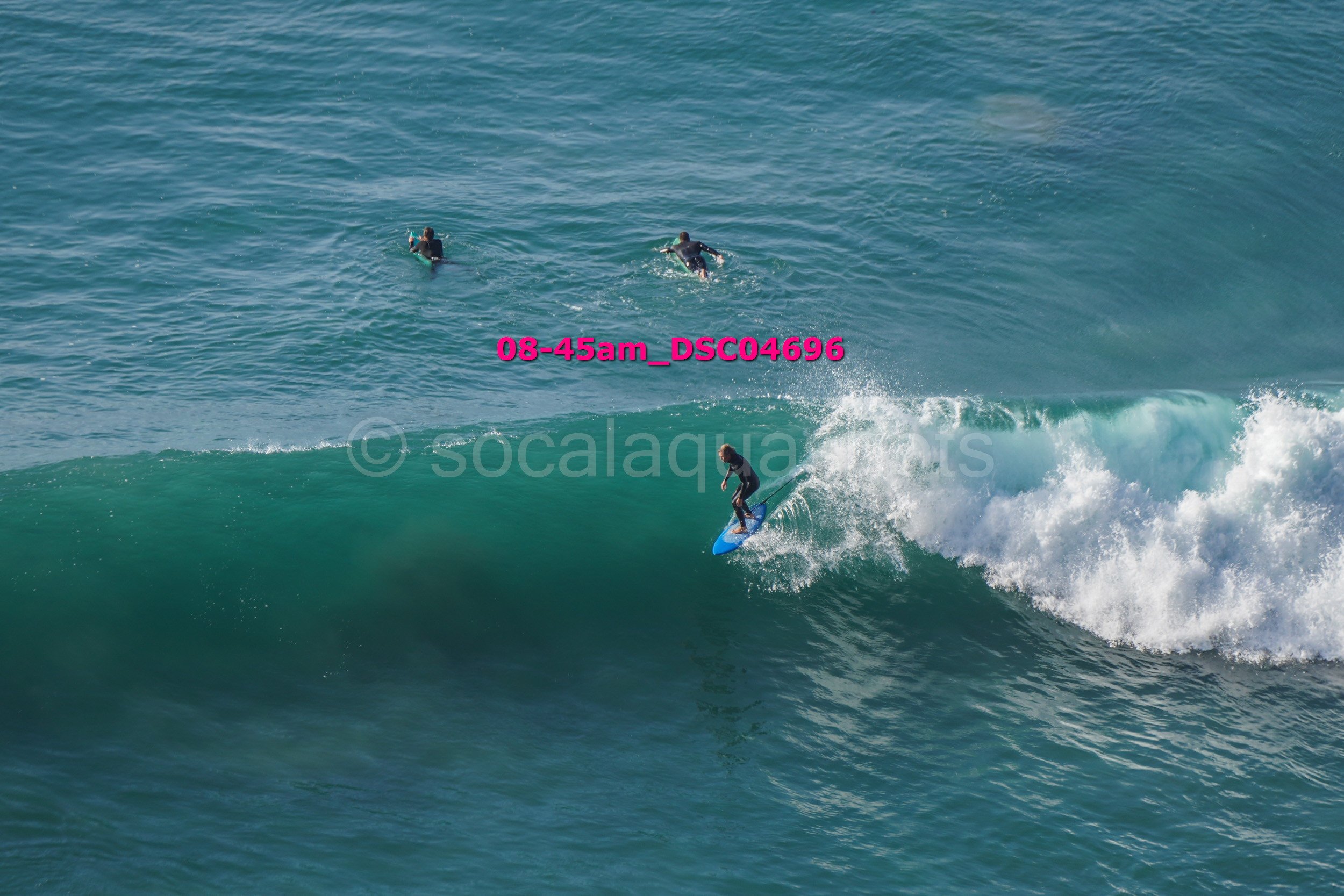 A surfer riding a large wave with three people in the water nearby.