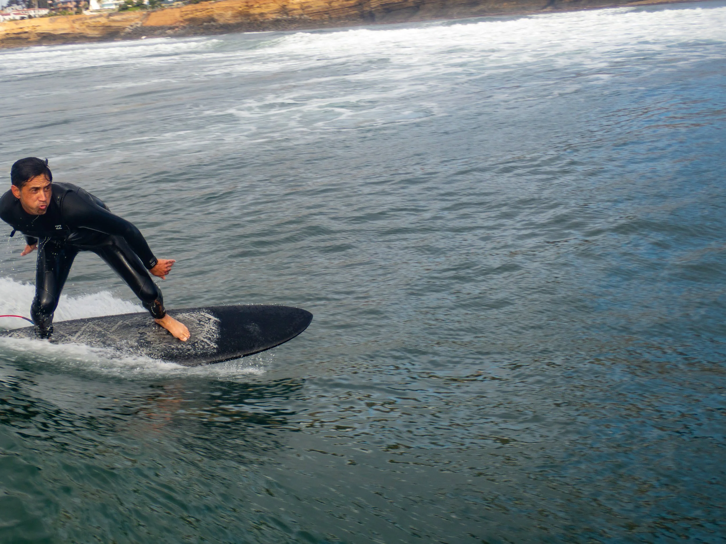 A man in a black wetsuit riding a surfboard on the water.