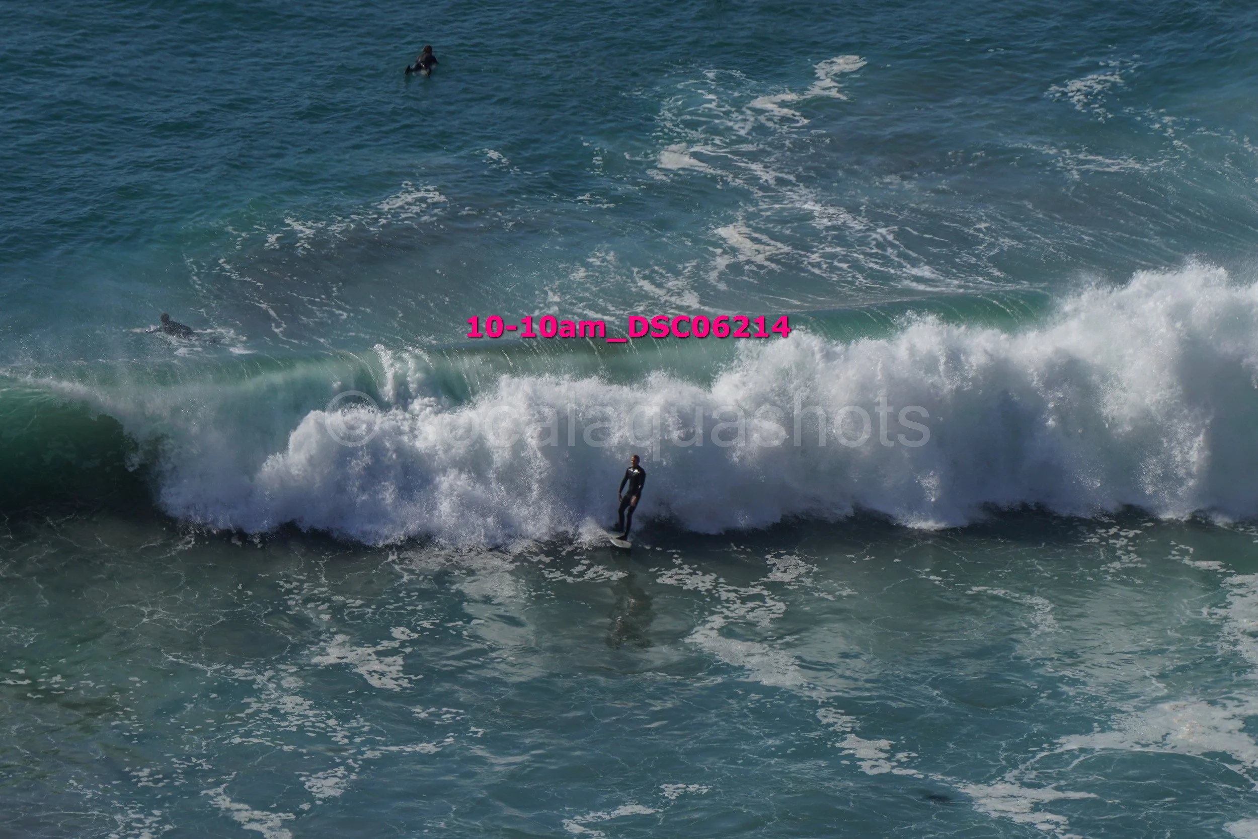 A person surfing on a wave in the ocean, with several surfers visible in the background.