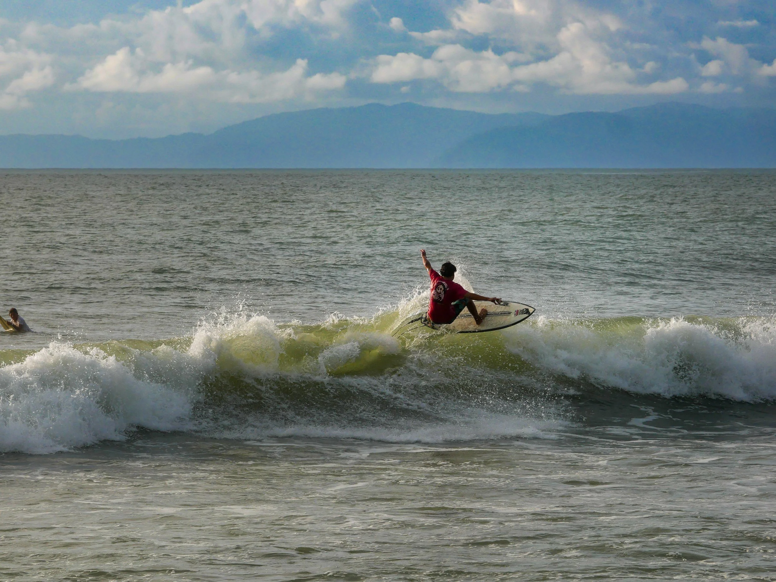 Surfer riding a wave in the ocean with mountains in the background