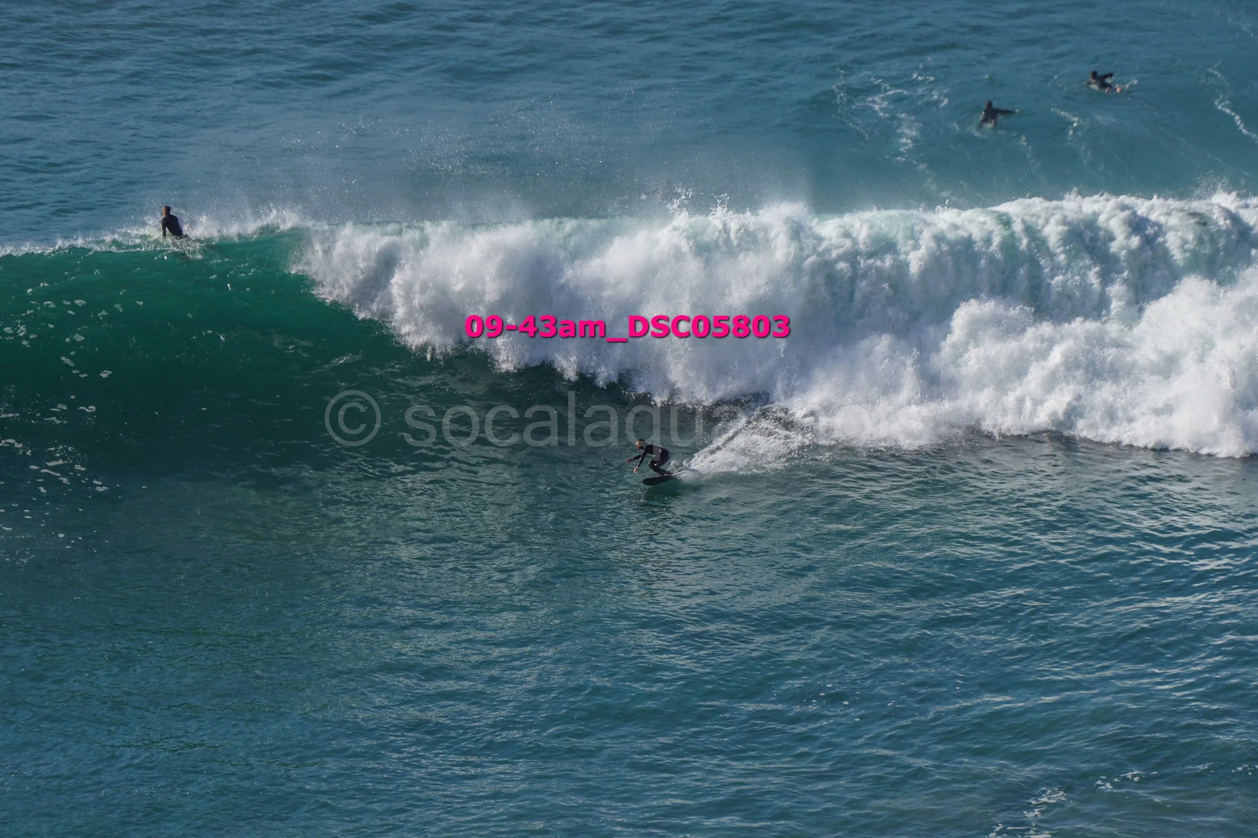 A person surfing on a large wave with several other surfers in the background in the water.