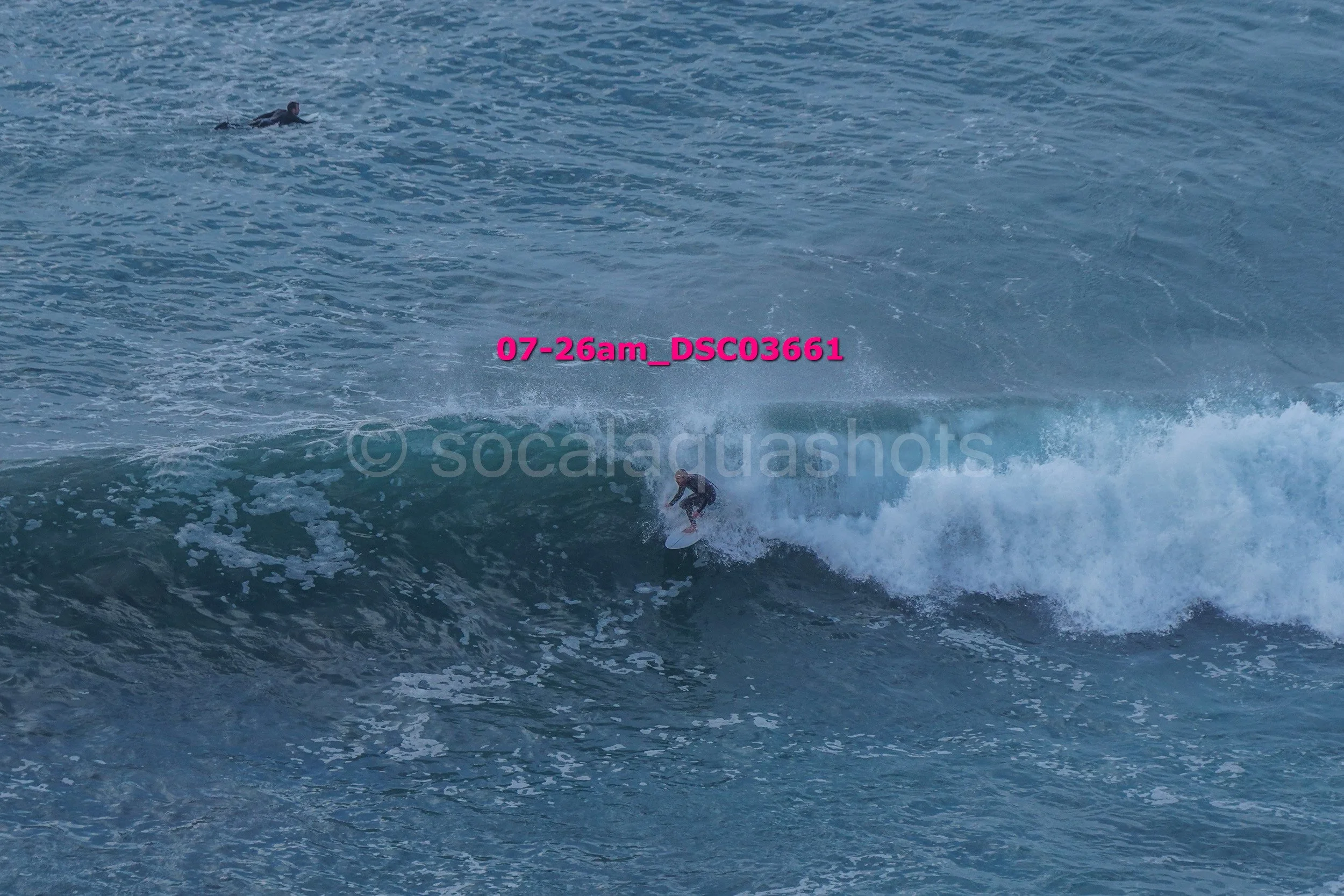 A person surfing on a wave in the ocean with another person swimming or floating in the water nearby.