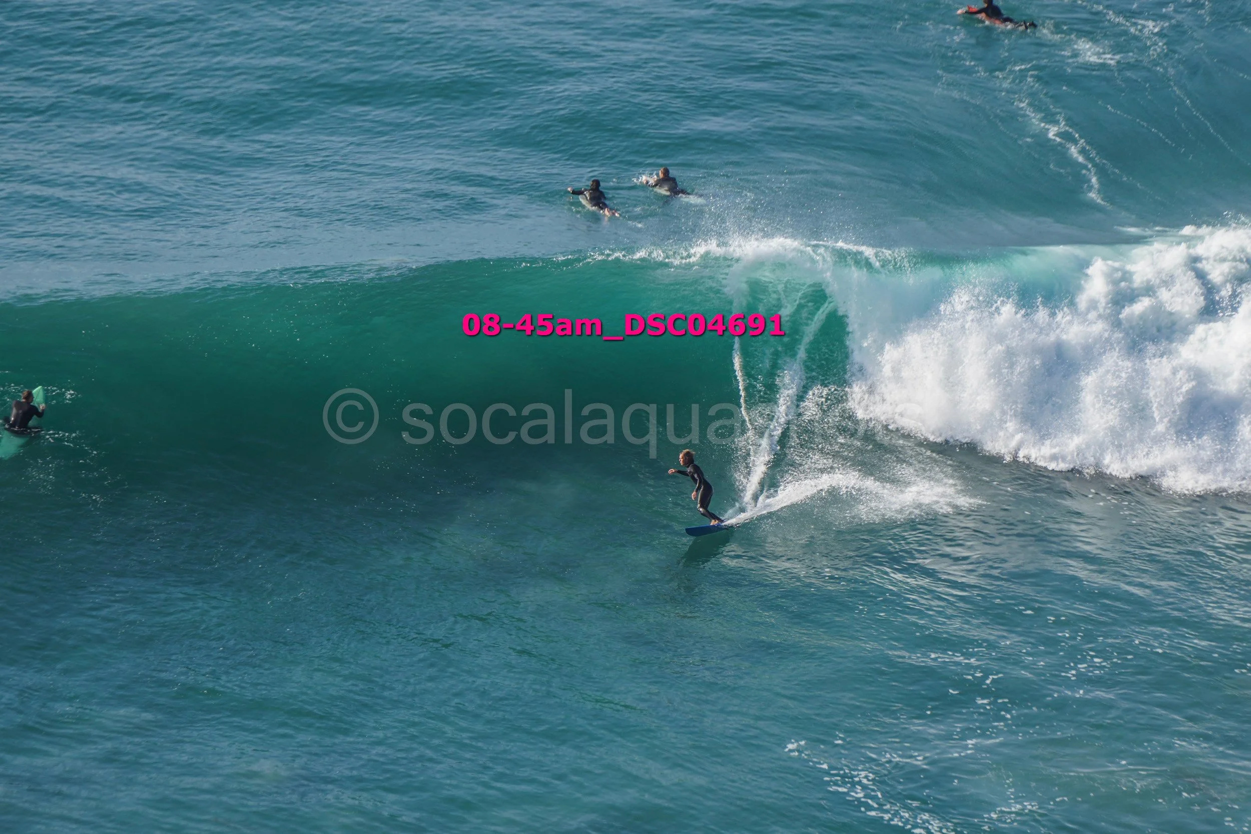 Surfer riding a large wave with two surfers paddling in the background.