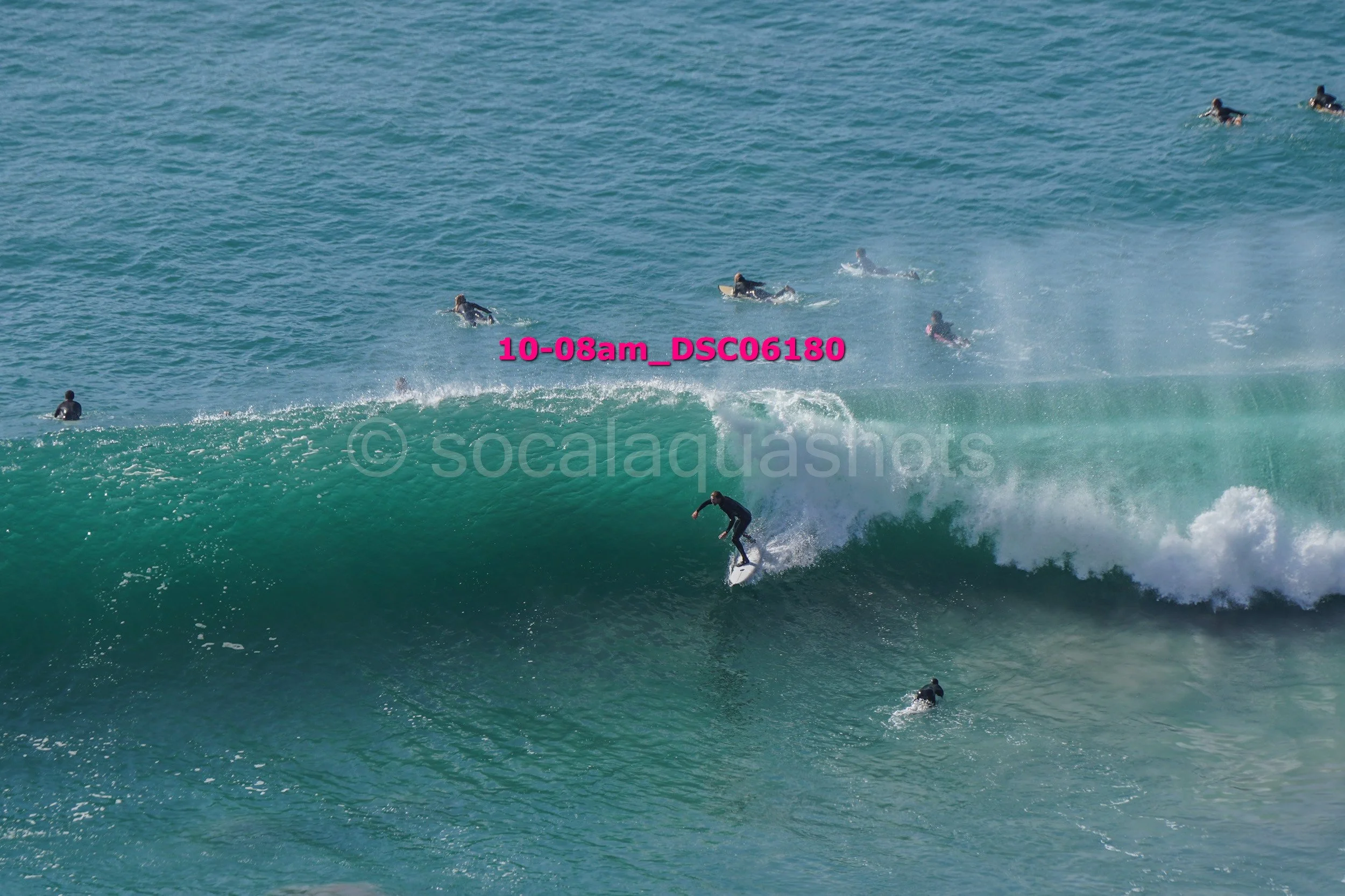 A surfer riding a large wave while several other surfers and swimmers are in the water nearby.