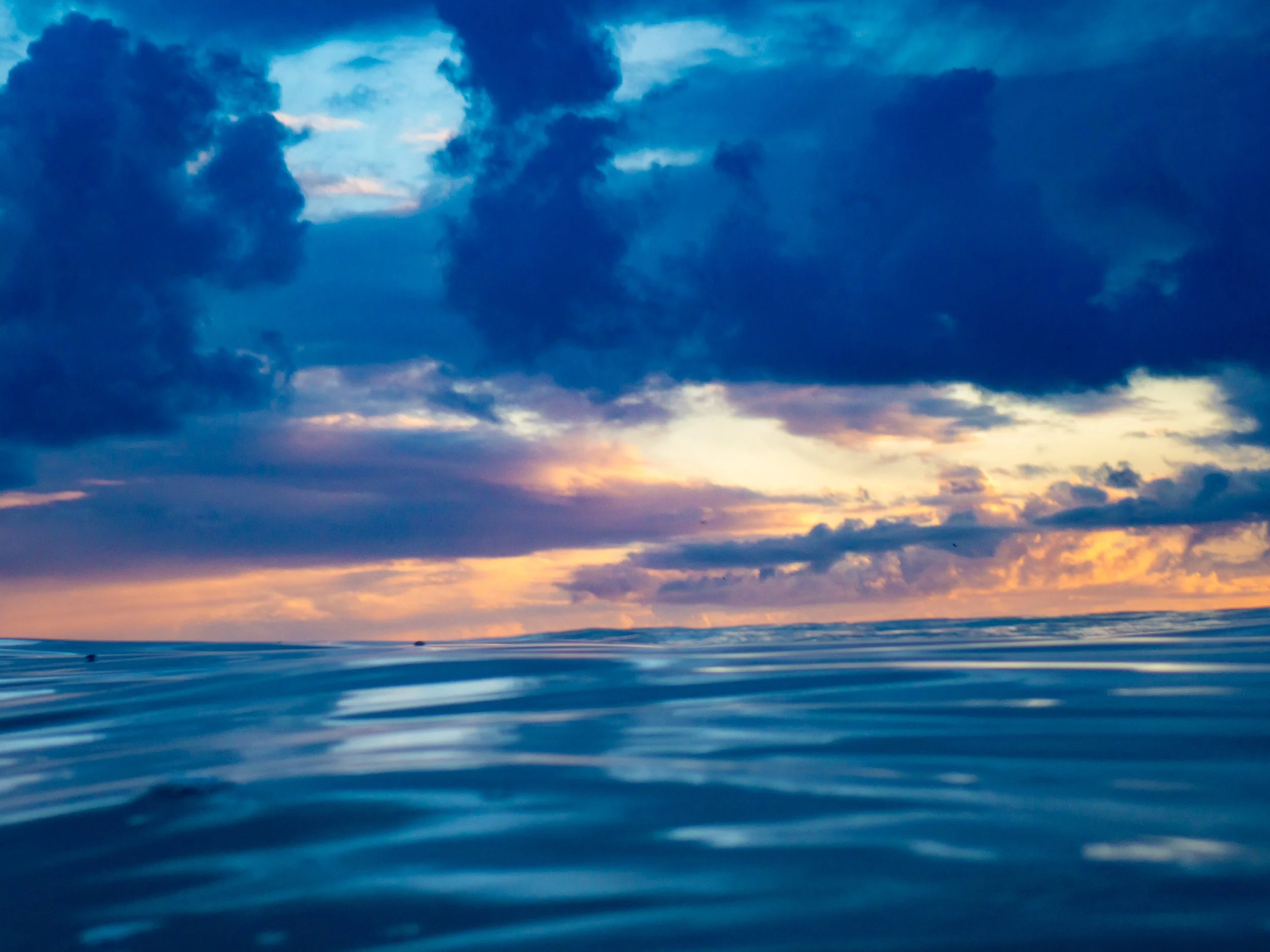 Calm ocean water with a sunset sky filled with dark clouds and hints of orange and pink hues.