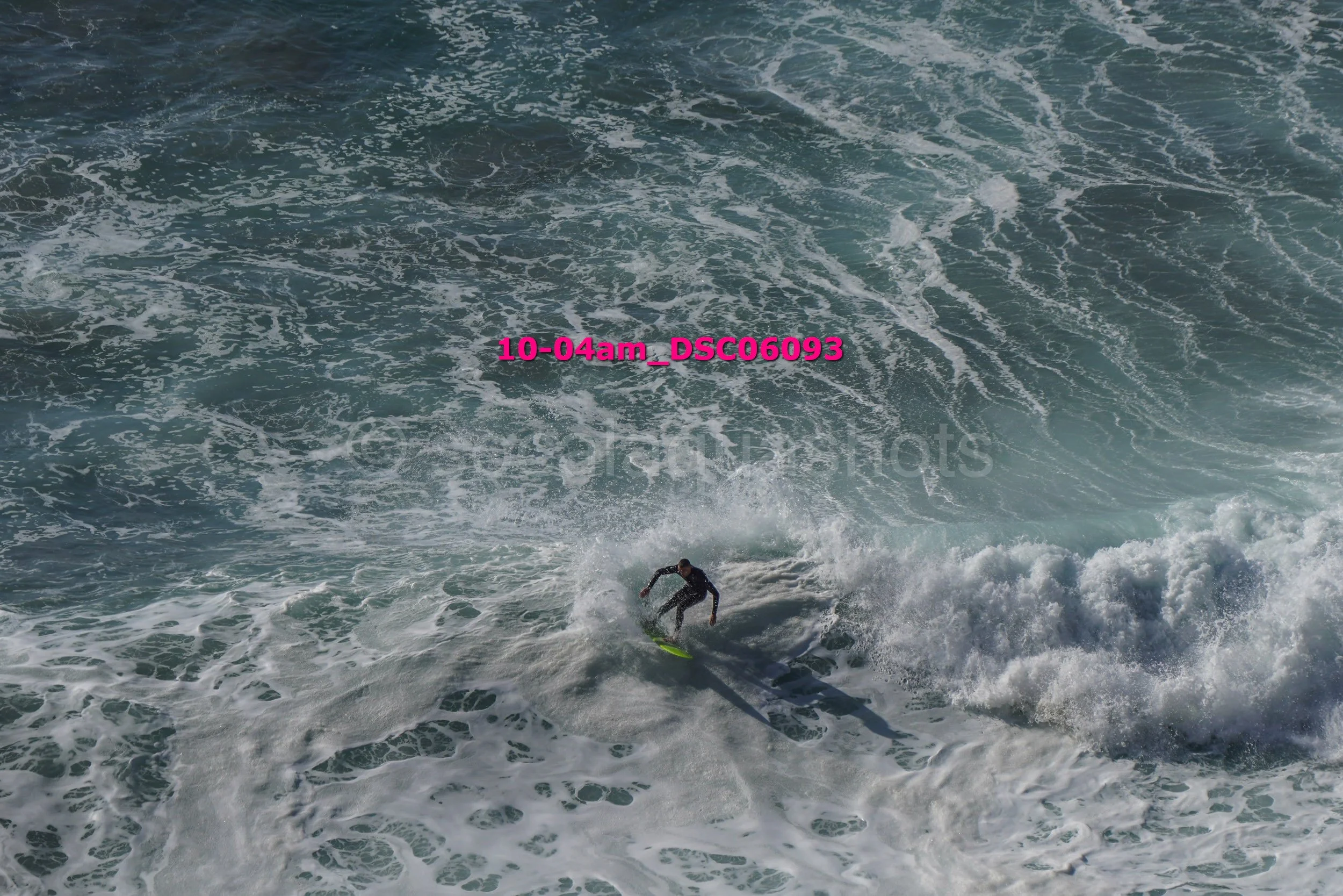 A surfer riding a wave in the ocean with white foam and water spray, under a bright sky.