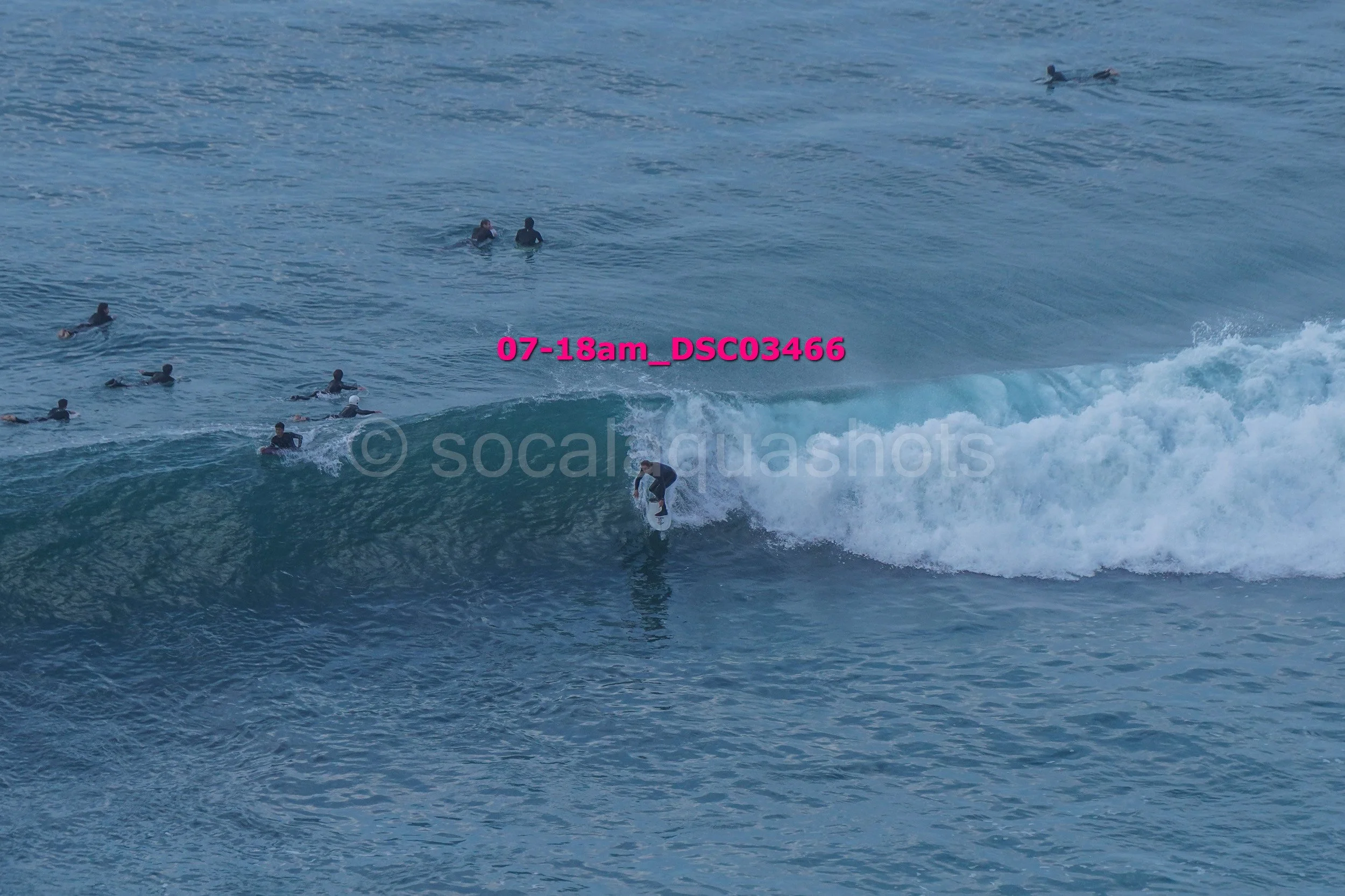 A person surfing on a wave near several other surfers in the water.