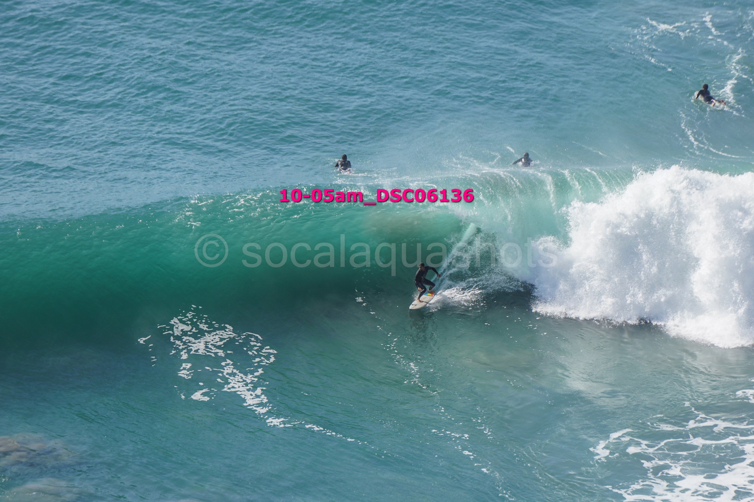 A person surfing on a large wave in the ocean with several other surfers in the background.