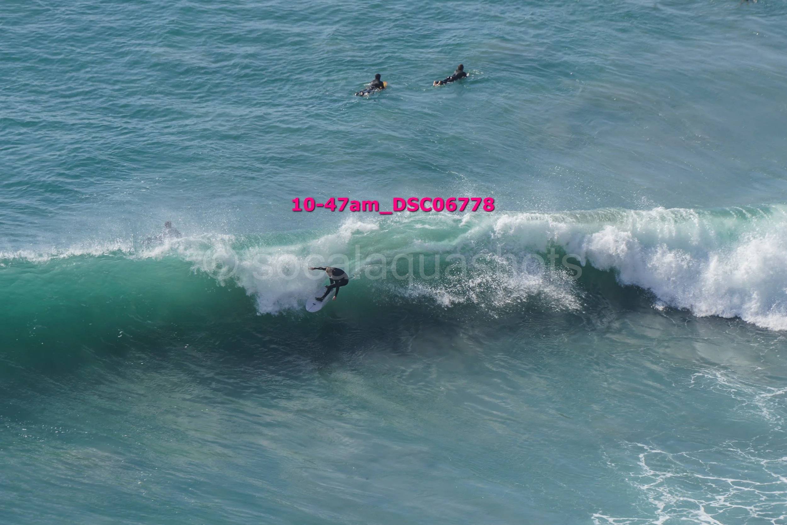 A person surfing on a wave with three other people swimming in the background.