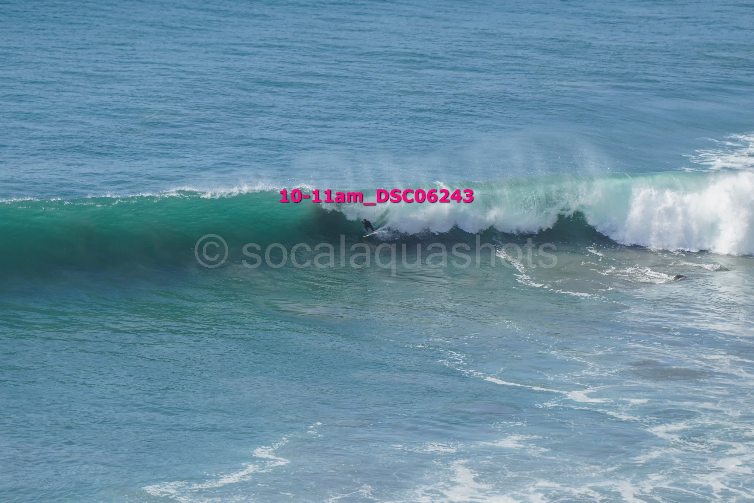 A person surfing on a large wave in the ocean with blue water and white foam at the crest.