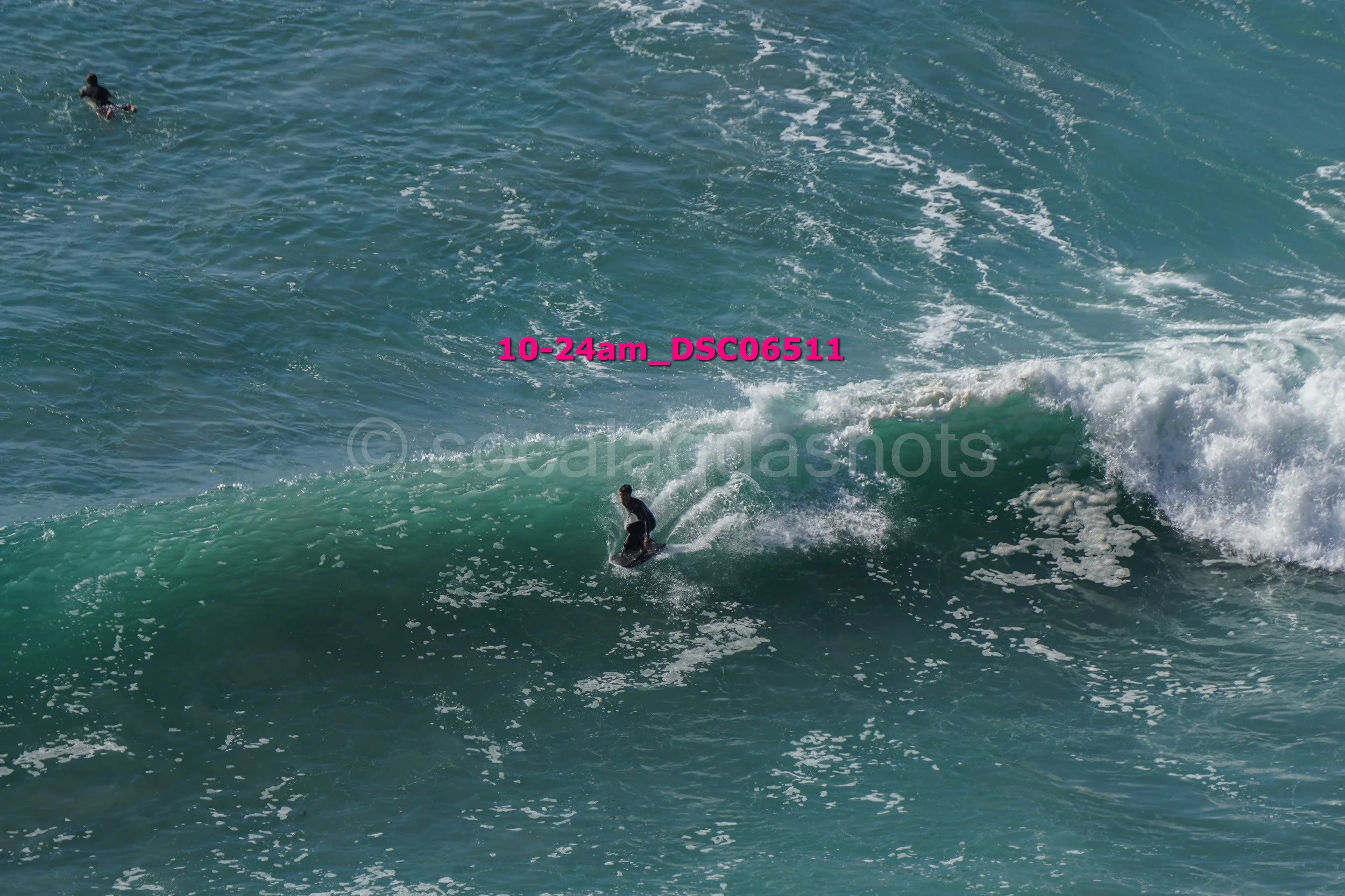 Person surfing on a wave in the ocean, with another person swimming farther away.