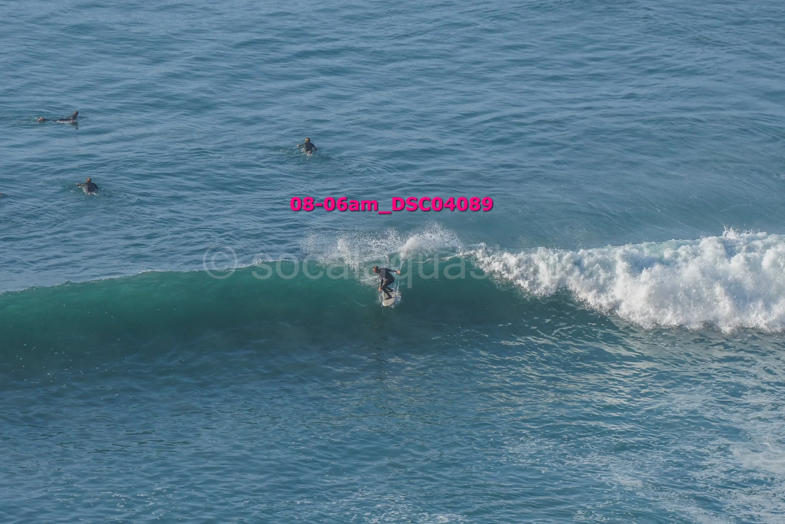 A person surfing on a wave in the ocean with four other surfers visible in the distance.