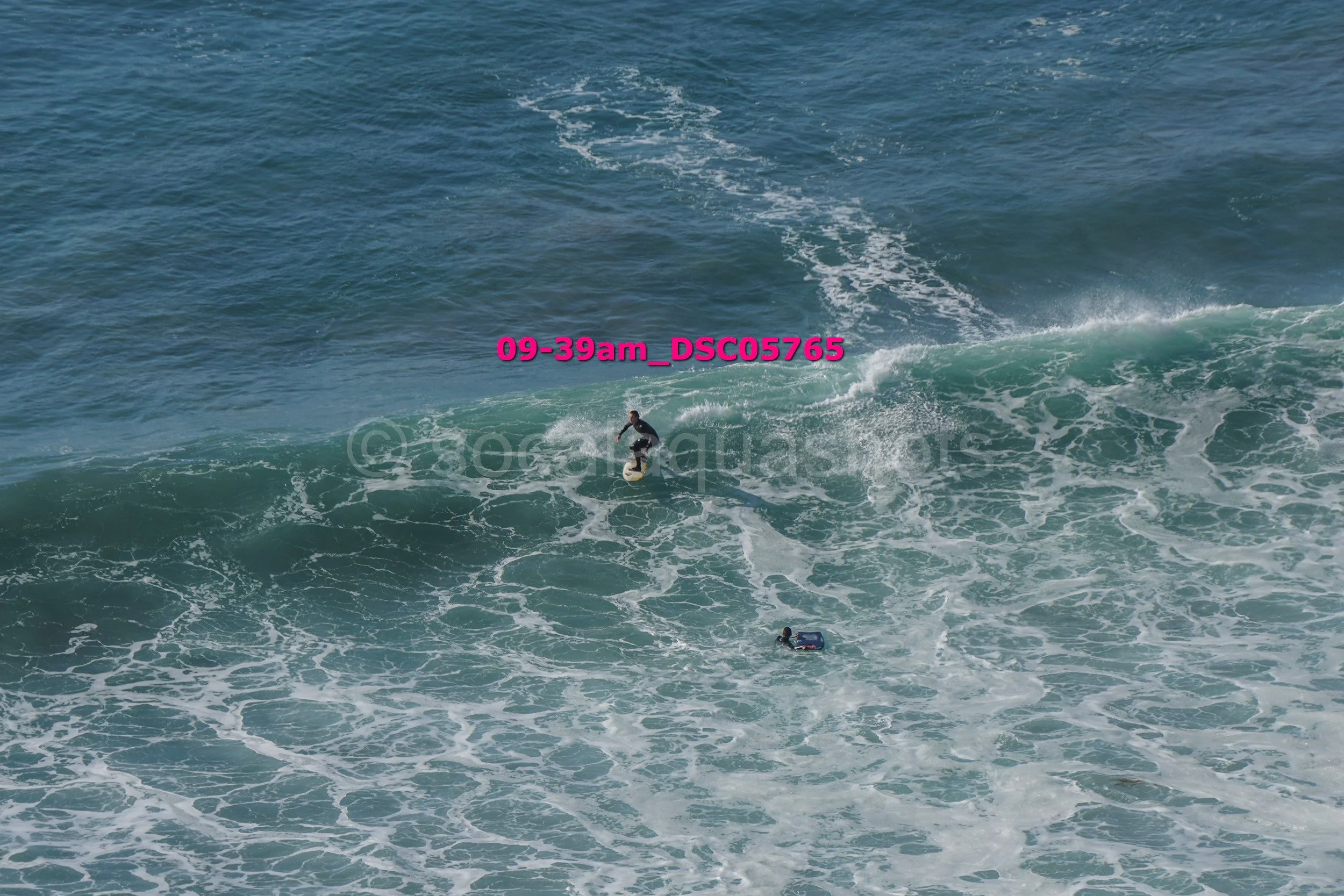 A person surfing on a wave in the ocean with another person floating nearby.