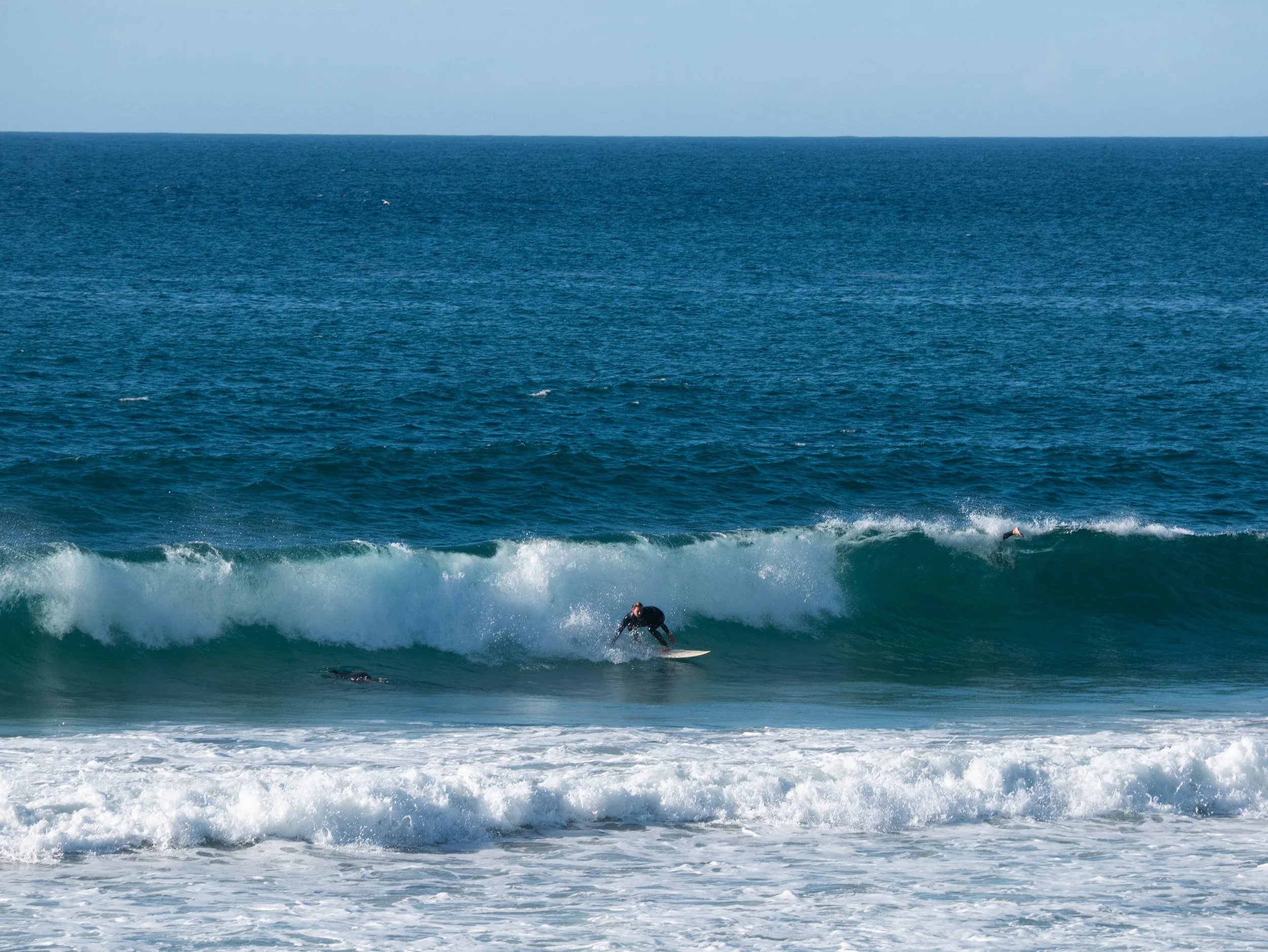 Surfer riding a wave in the ocean with other surfers in the distance.
