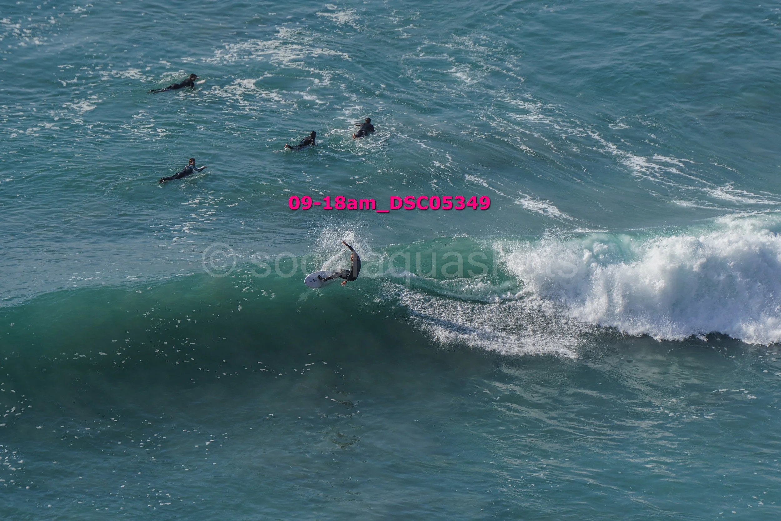 Surfer riding a wave with several people swimming in the background.
