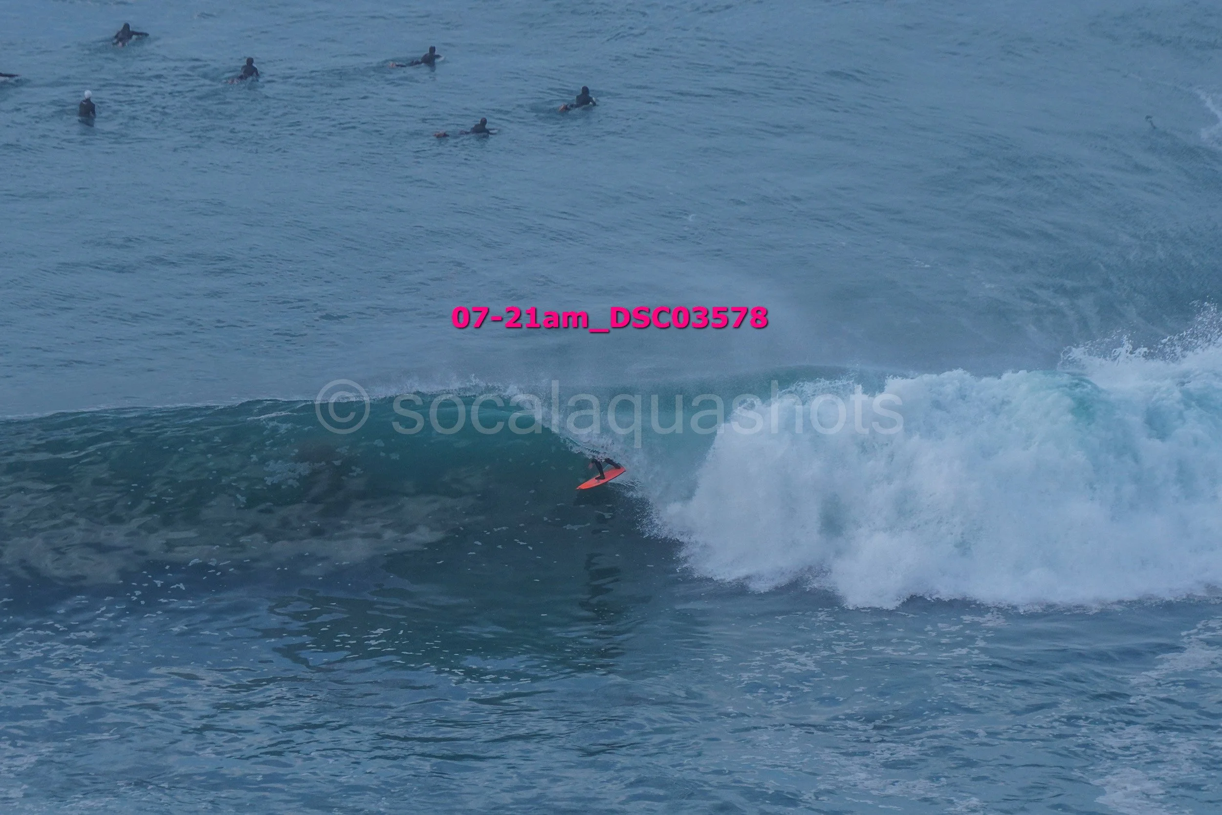 Surfer riding a wave with a group of swimmers in the background in the ocean.