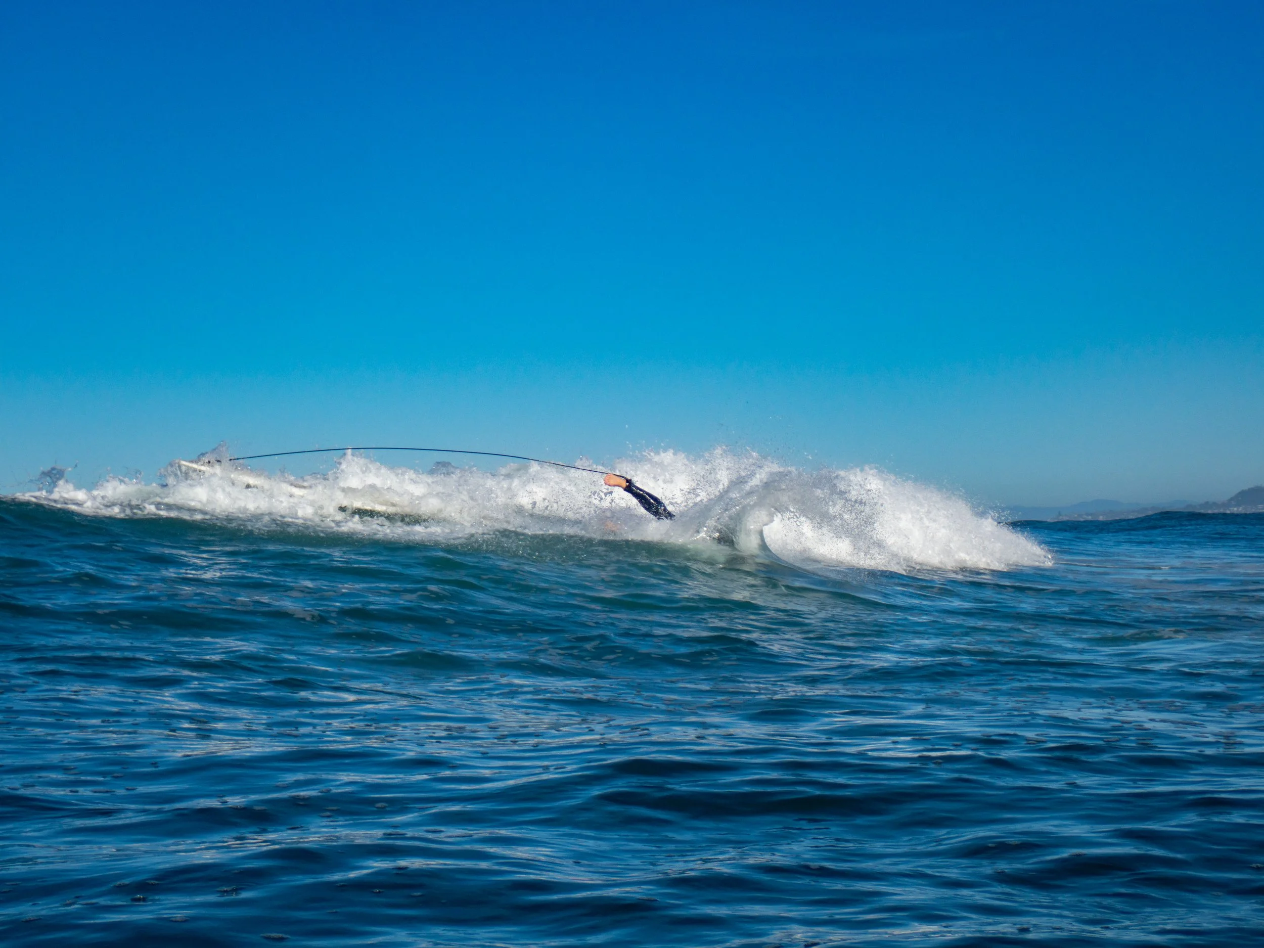 A person is surfing on a wave in the ocean under a clear blue sky.