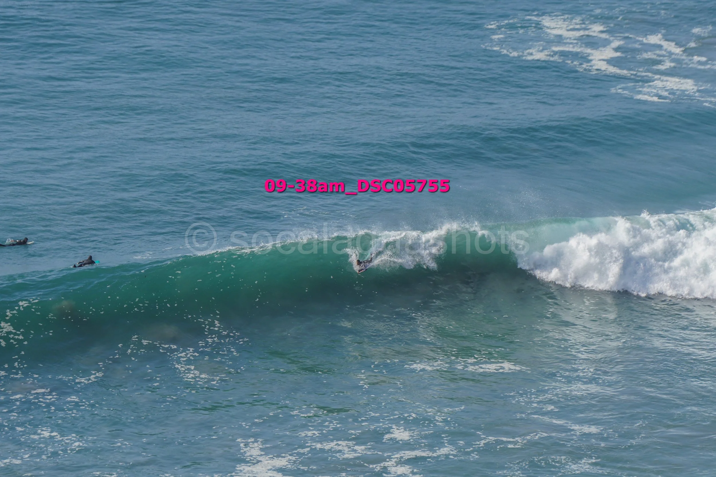 A person surfing a wave in the ocean, with other surfers visible in the water nearby.