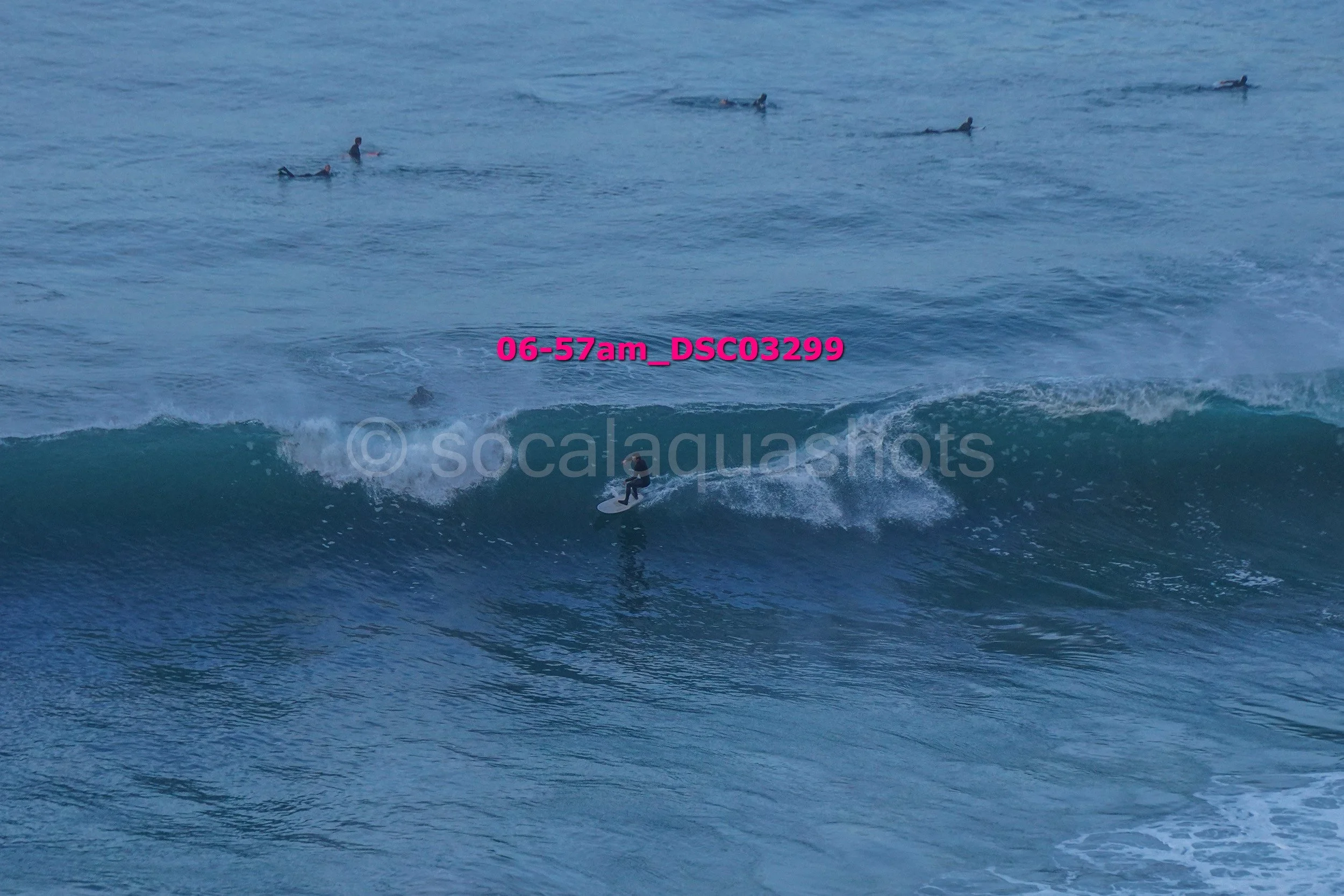 A person surfing on a wave in the ocean with multiple surfers in the background.
