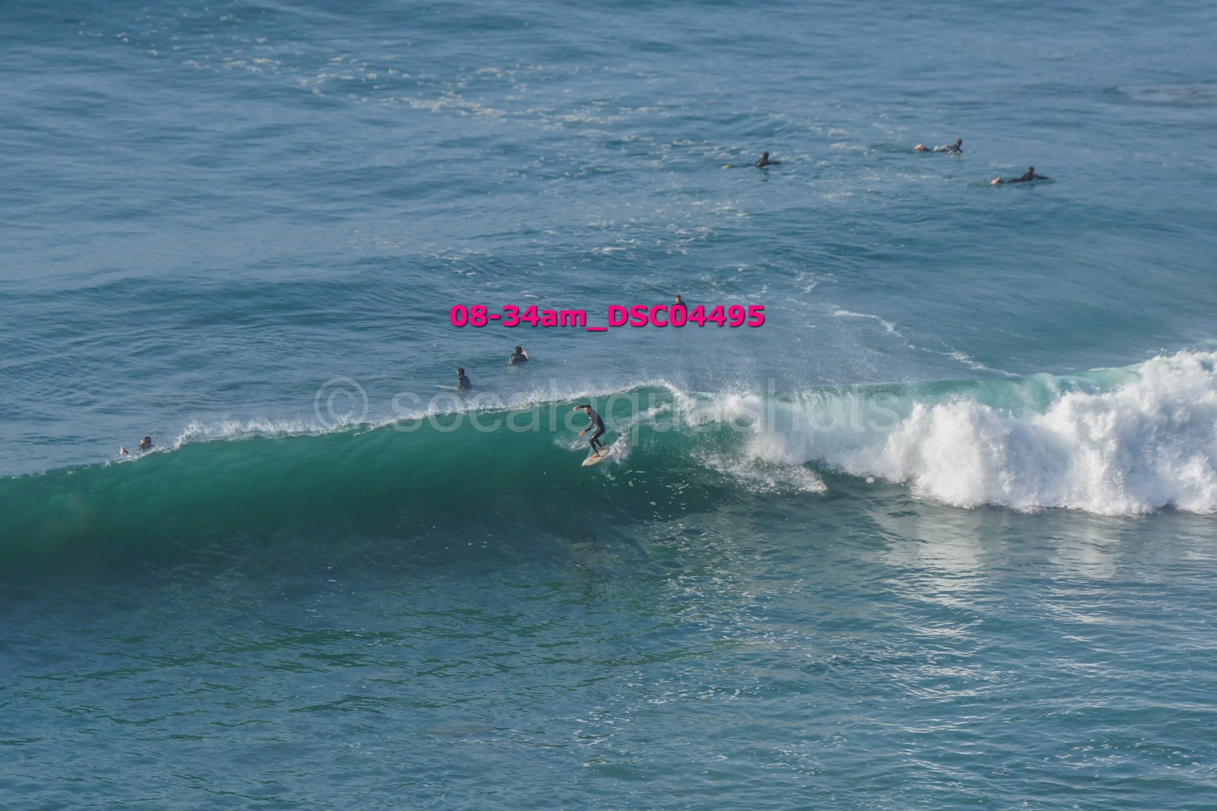 A person surfing on a wave with several other surfers in the water nearby.