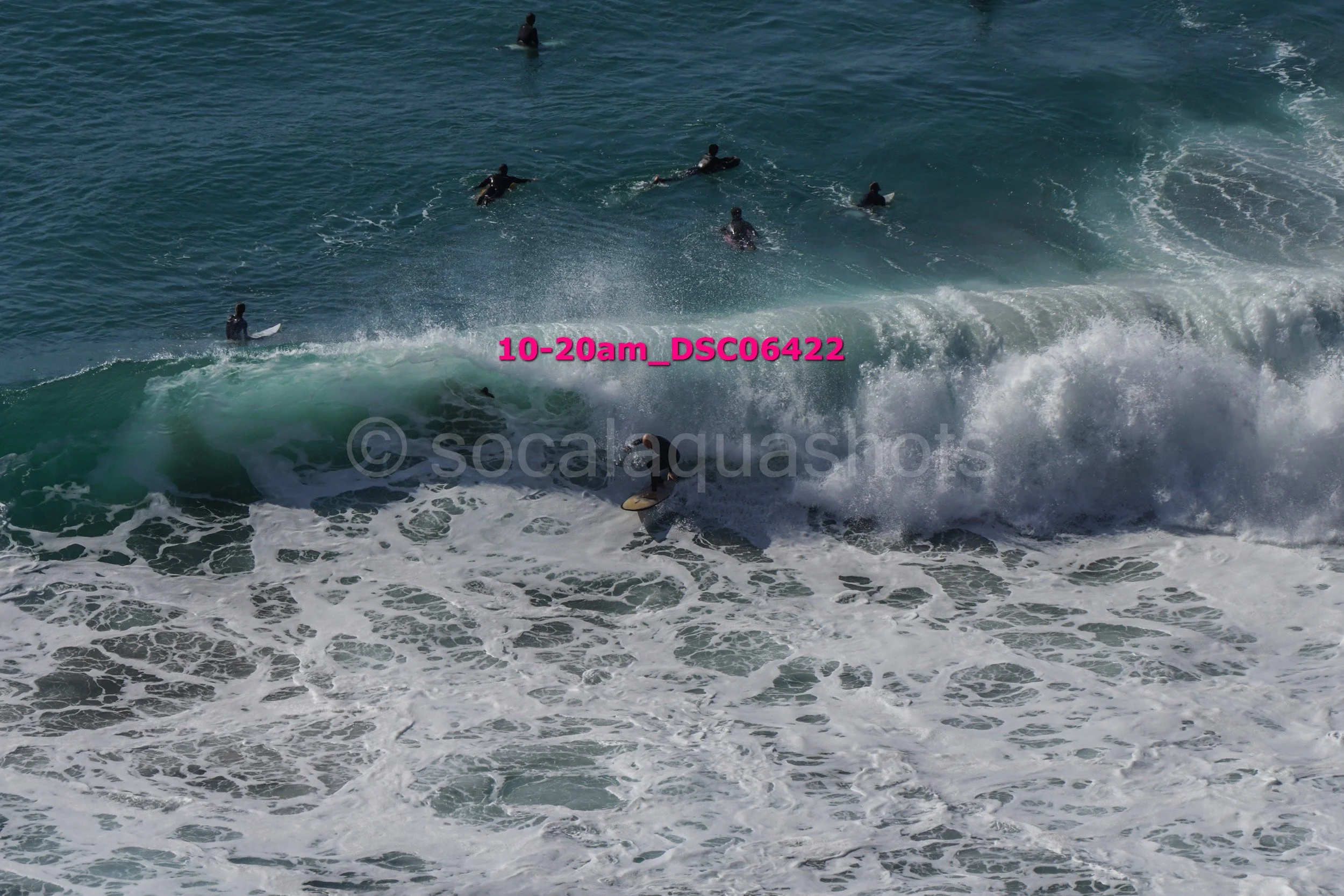 Surfer riding a wave with several people in the water in the background.