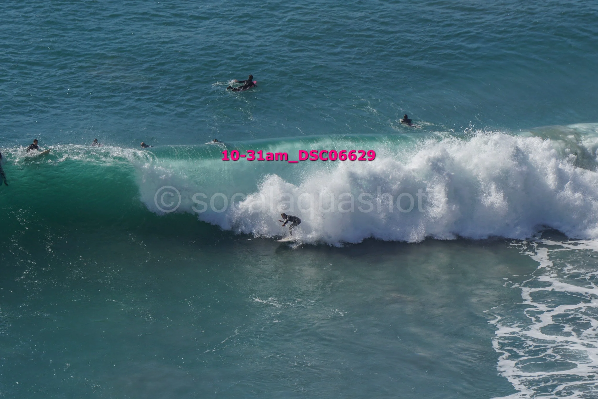 Surfers riding a large wave in the ocean with some surfers paddling on their boards in the background.