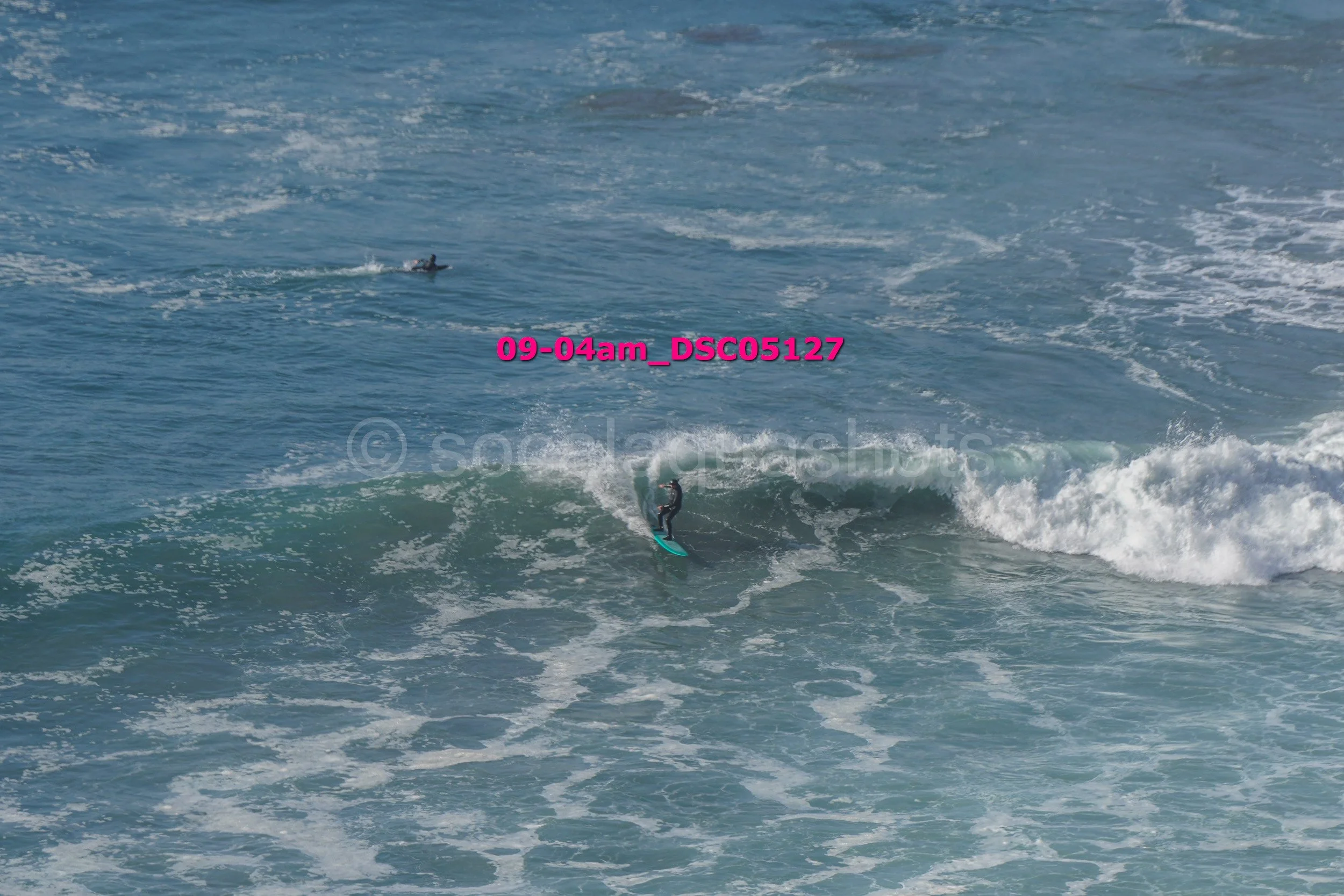 A person surfing on a wave in the ocean with another surfer in the background.