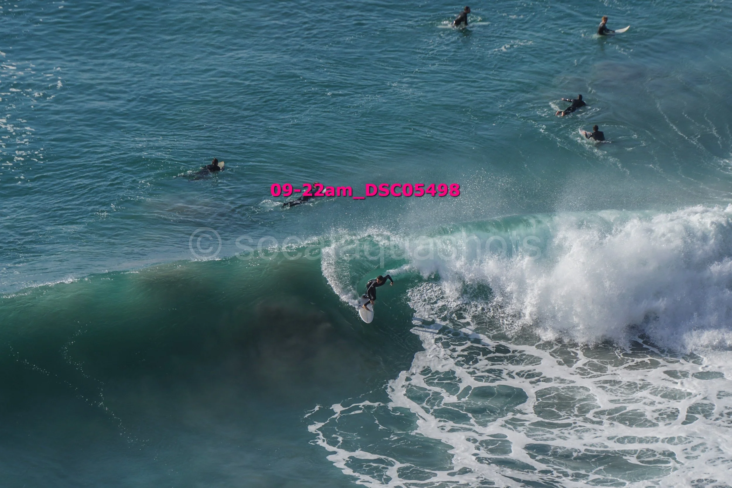 A surfer riding a large wave while several people surf in the background in the ocean.