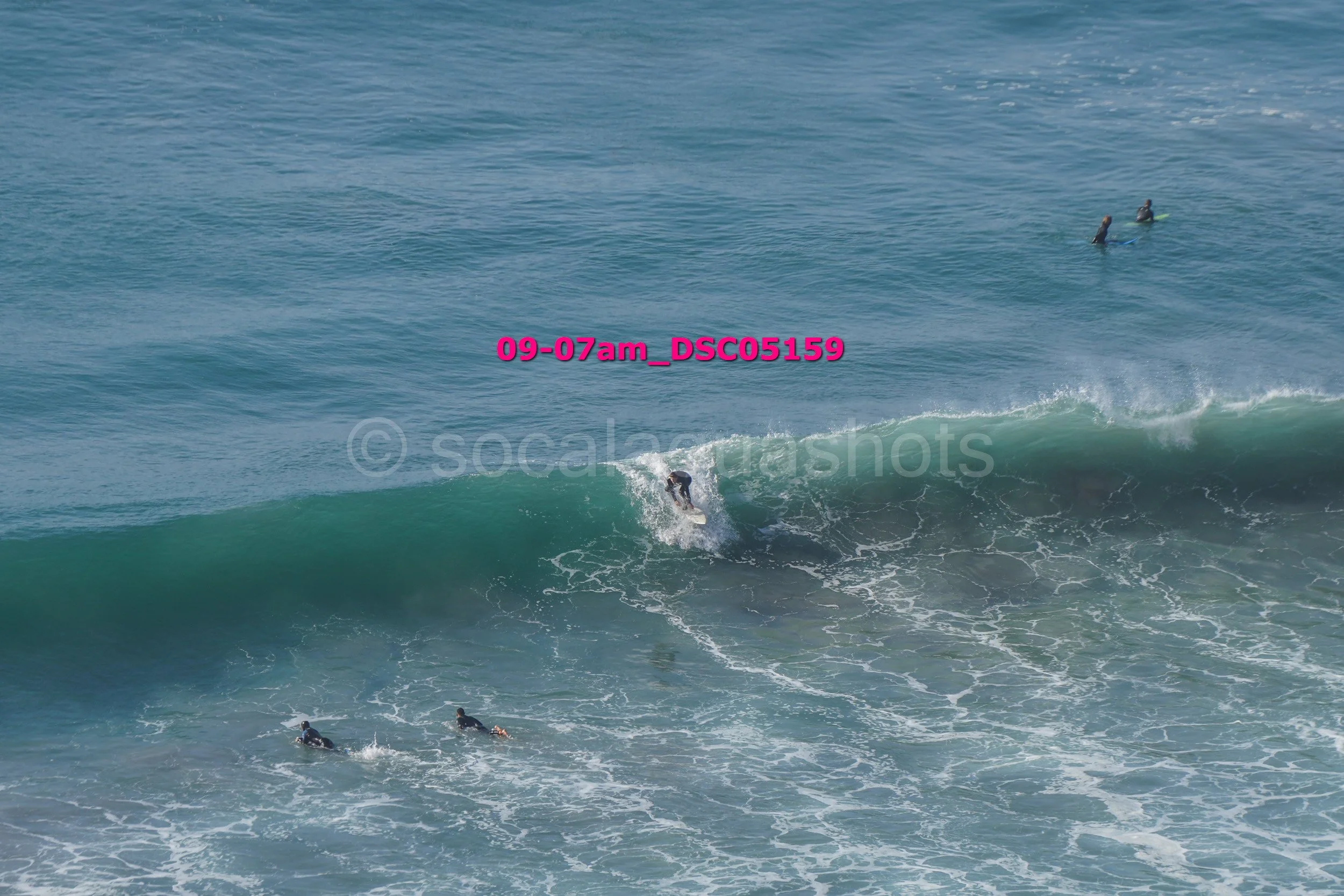 A person surfing a wave in the ocean with three other surfers in the water in the background.