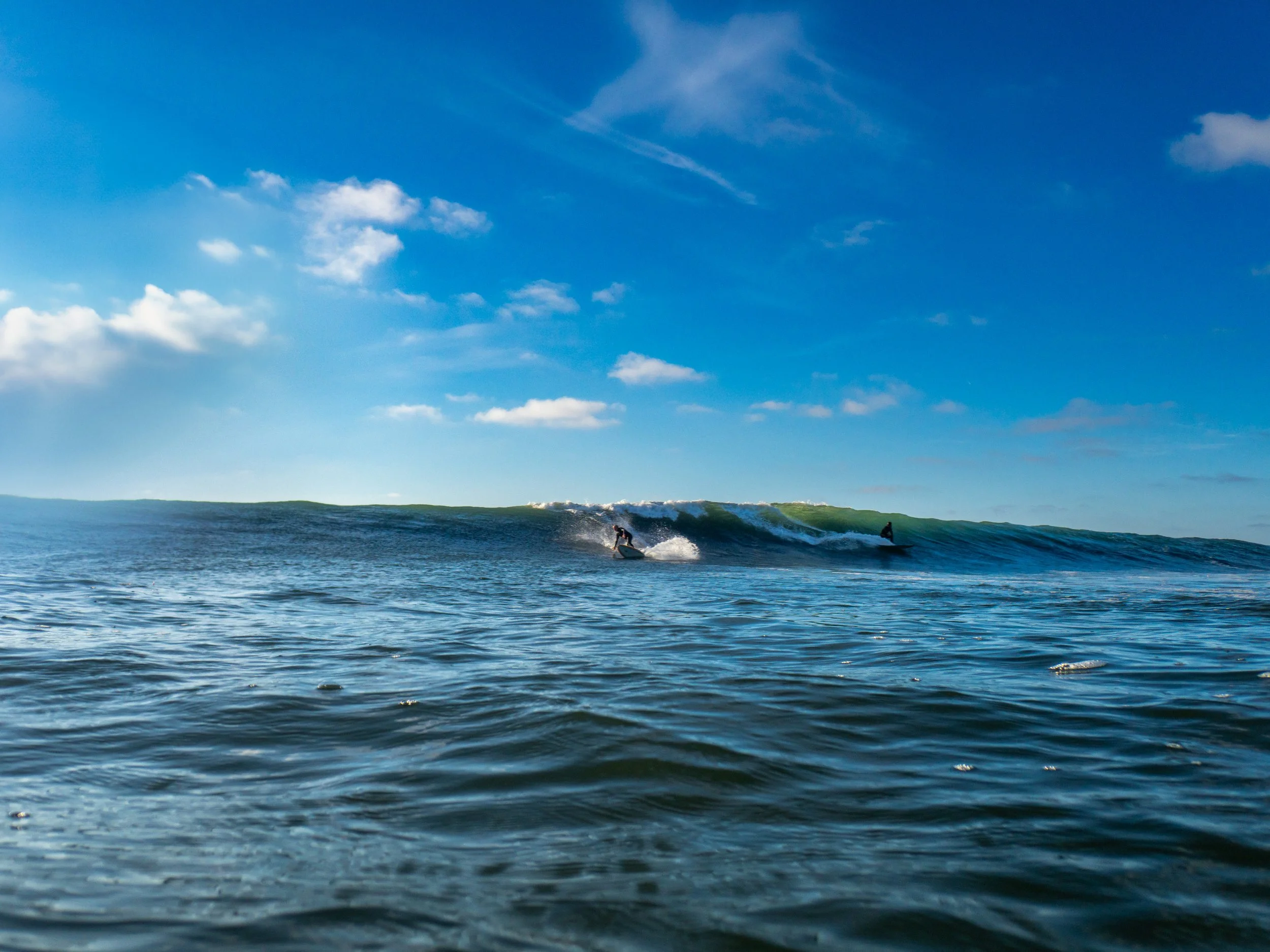 Two surfers riding waves in the ocean under a partly cloudy sky.