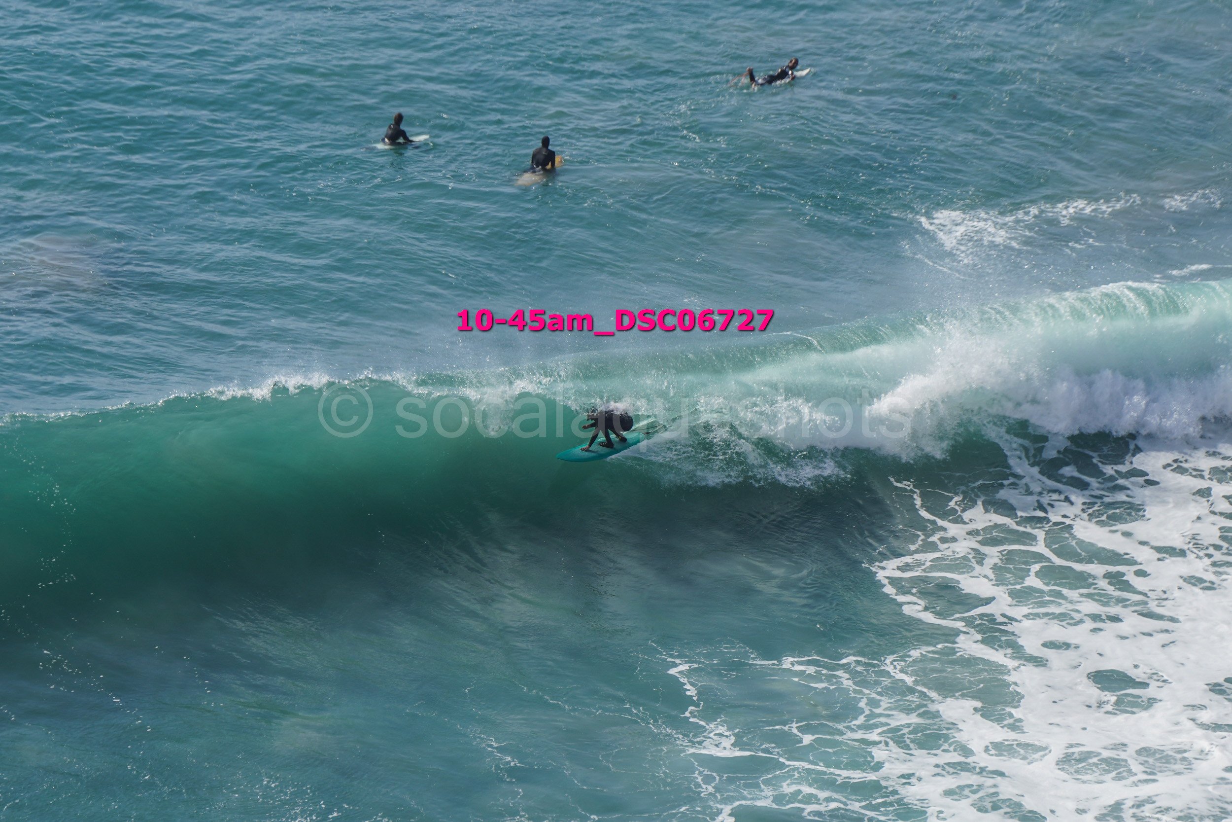 Surfer riding a wave with three surfers in the background in the ocean.