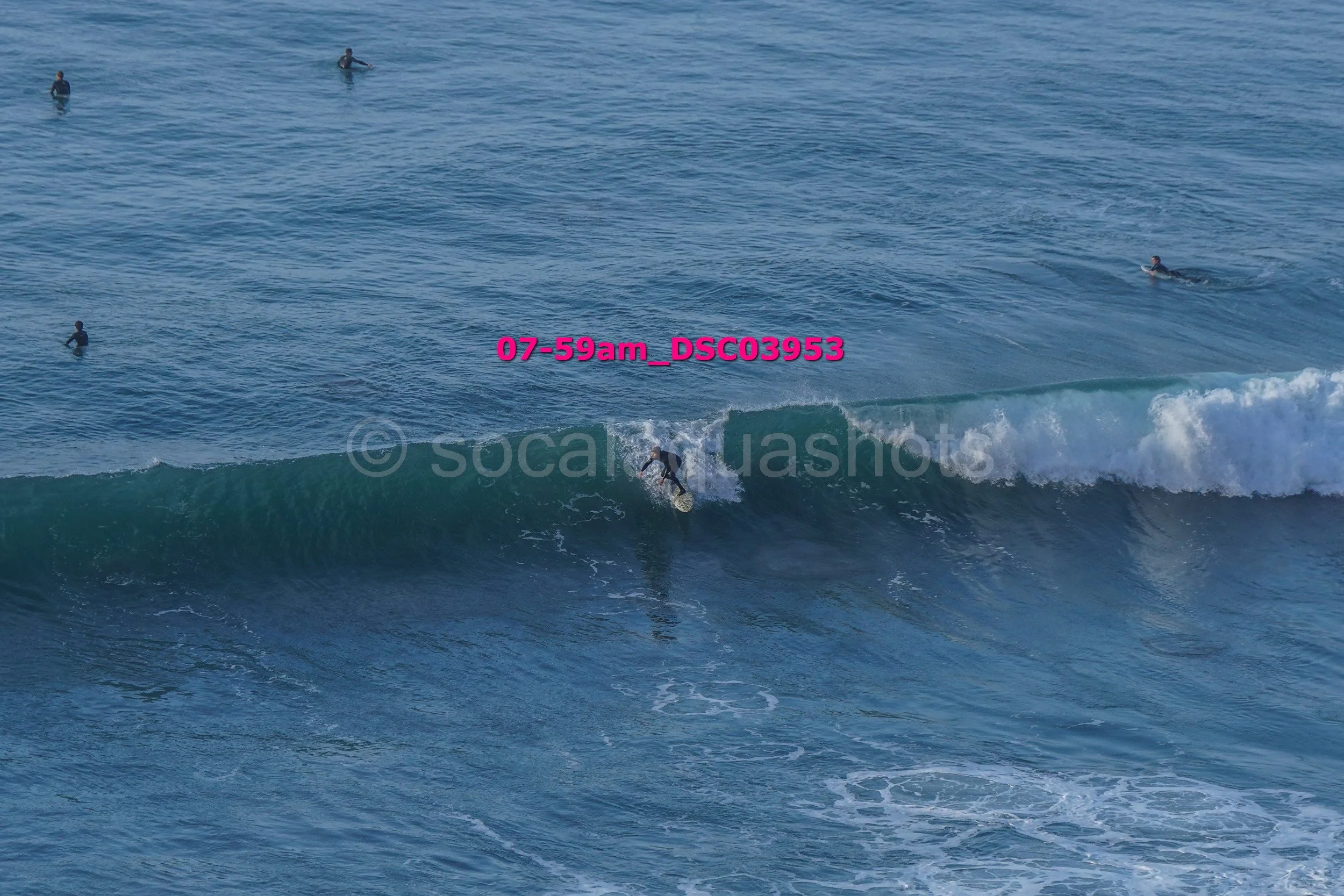 A surfer riding a wave in the ocean with several other surfers and people swimming in the water in the background.