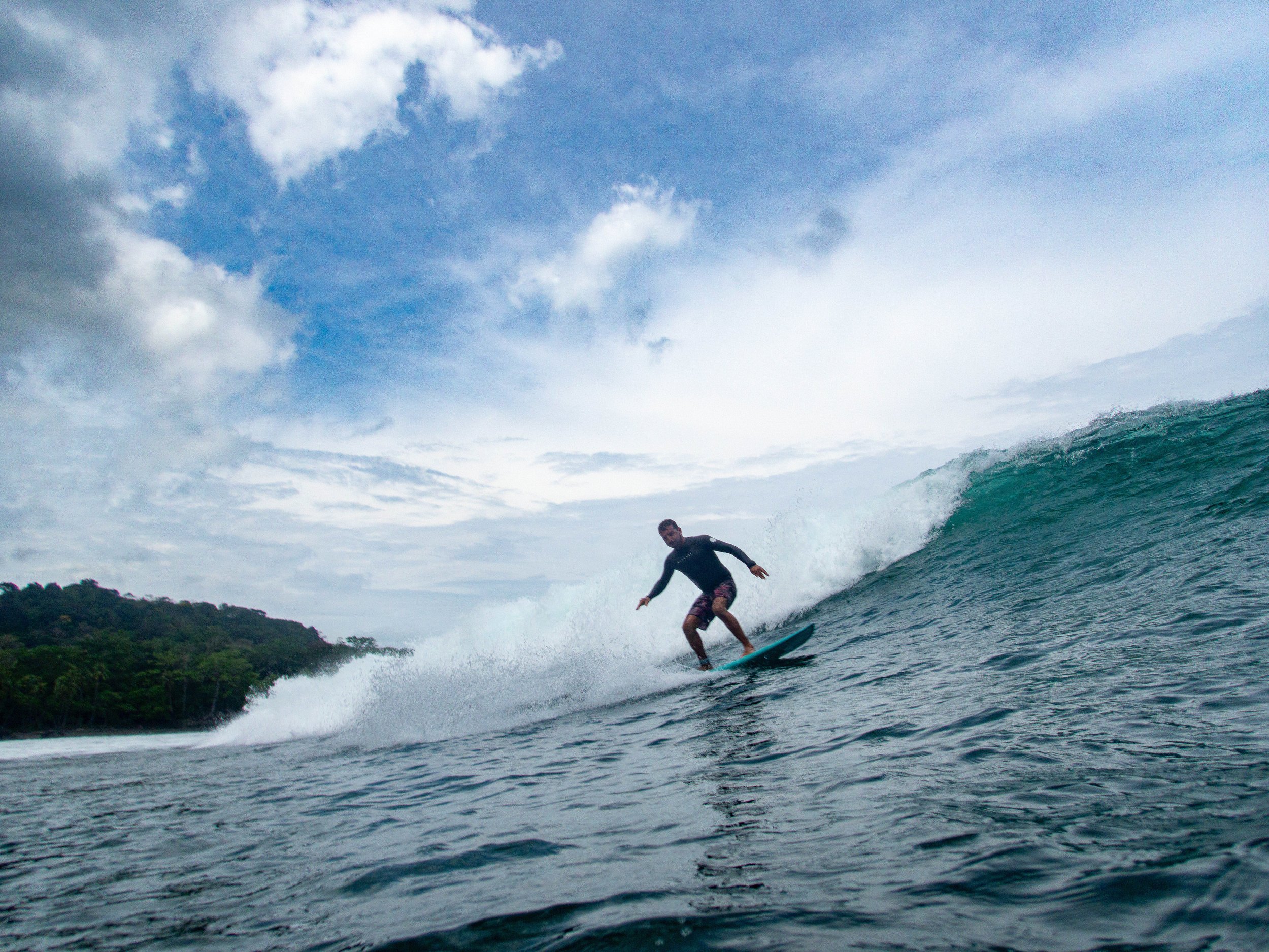 Surfer riding a wave in the ocean against a cloudy sky backdrop
