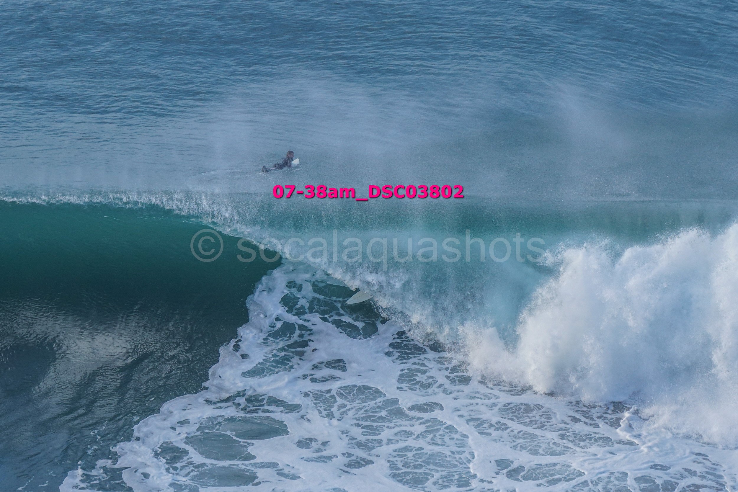 A surfer paddling in the ocean near a large wave.