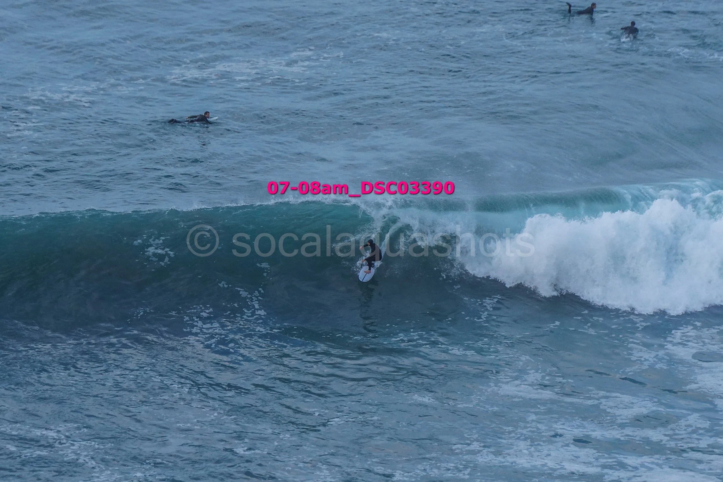 Surfer riding a wave near the shoreline with several people swimming in the background.