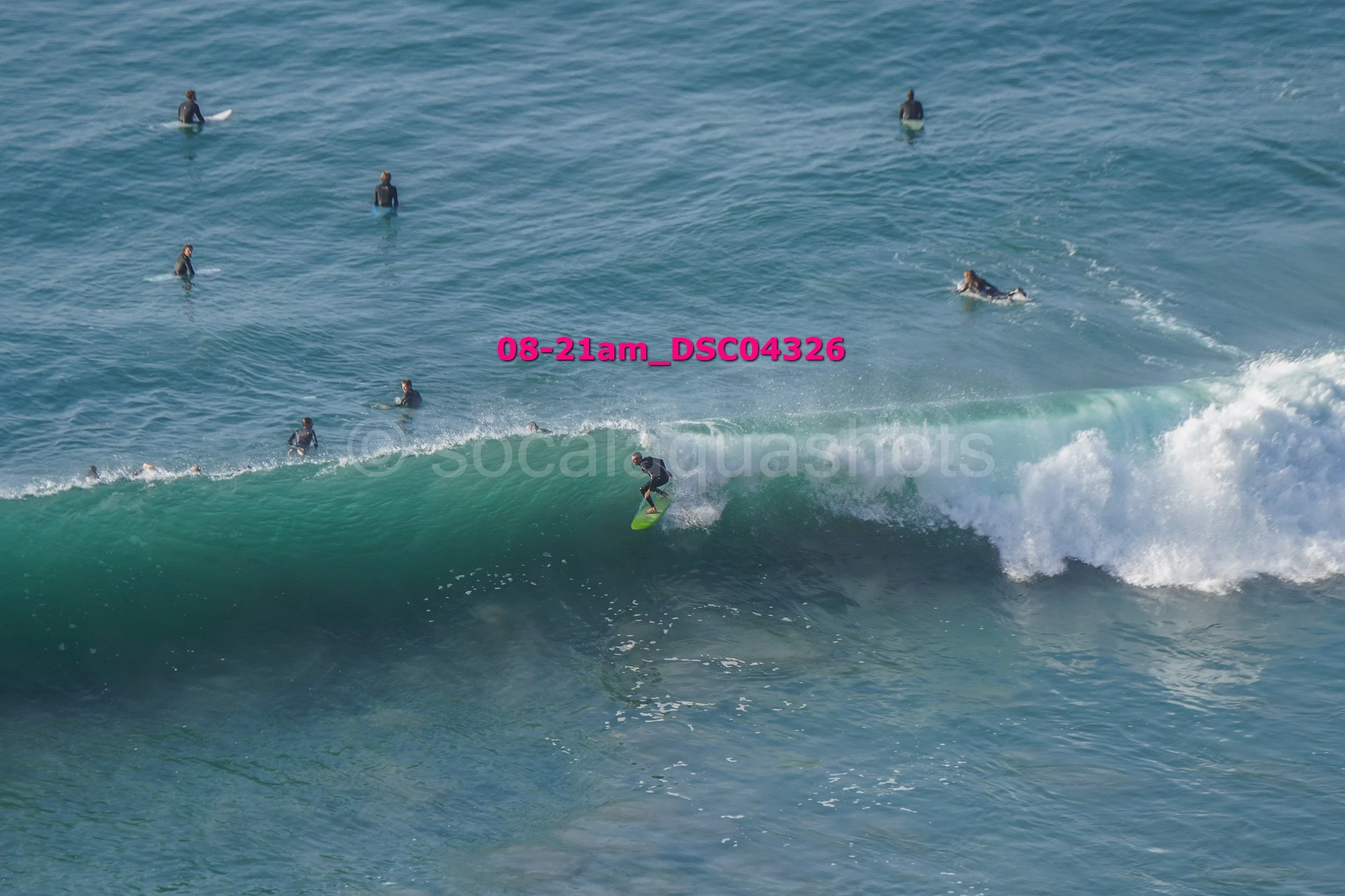 A person surfing on a wave while multiple surfers float in the ocean in the background.