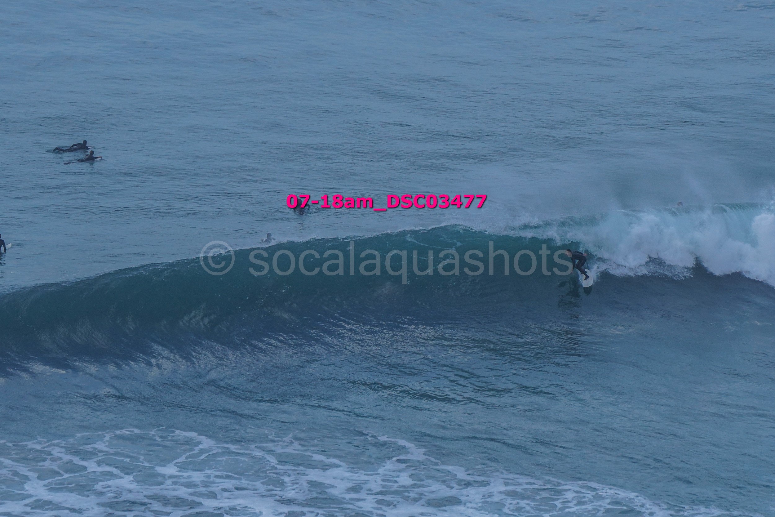 Surfer riding a wave in the ocean while other surfers wait in the water.