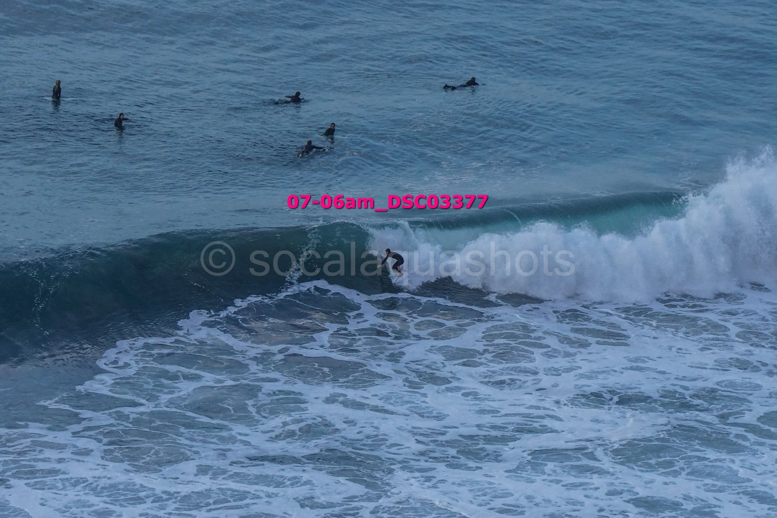 Surfer riding a wave with several people swimming in the ocean in the background.