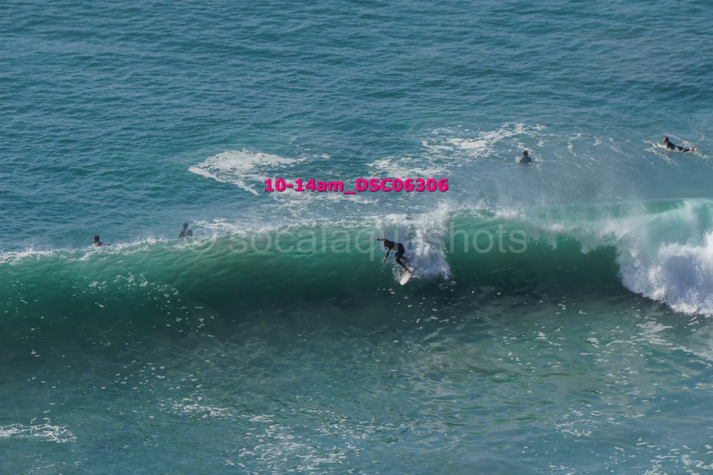 A surfer riding a wave in the ocean with several other surfers or swimmers in the background.