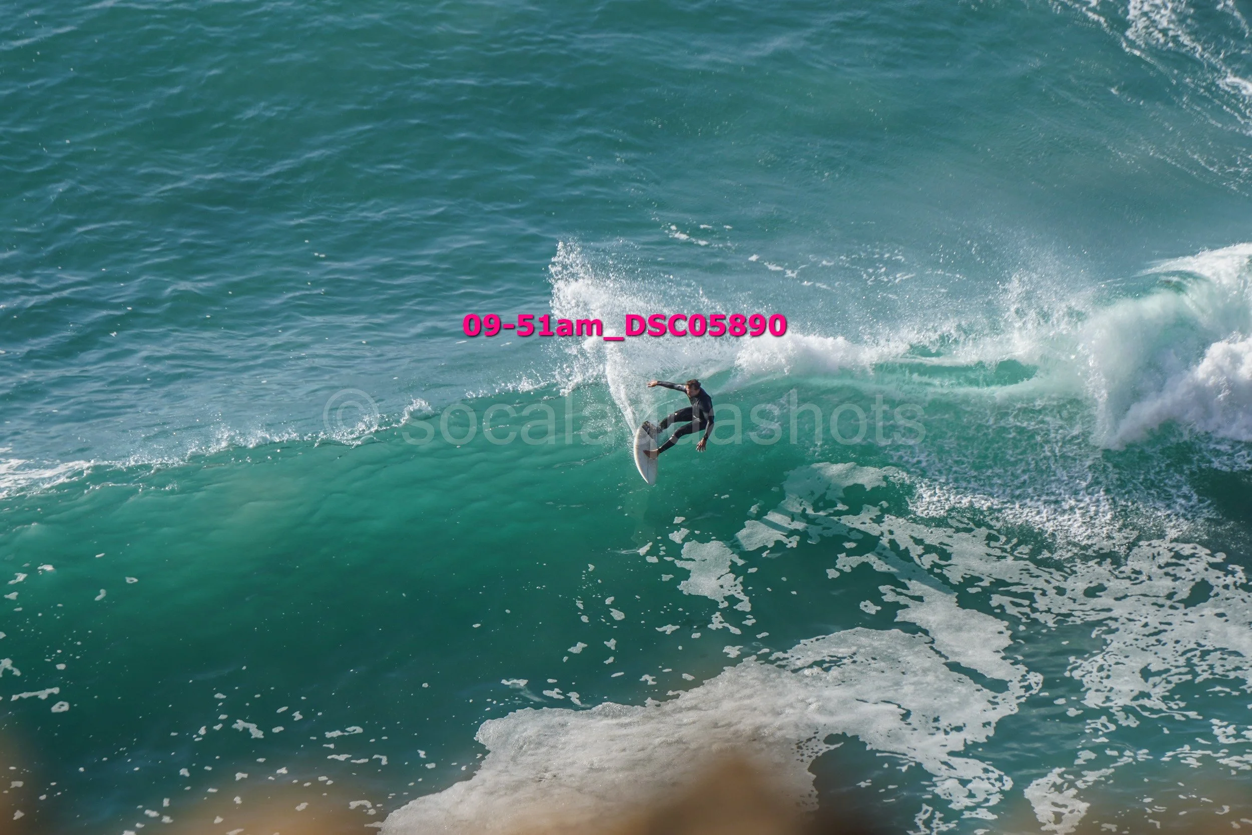 A person surfing on a wave in the ocean, wearing a black wetsuit.