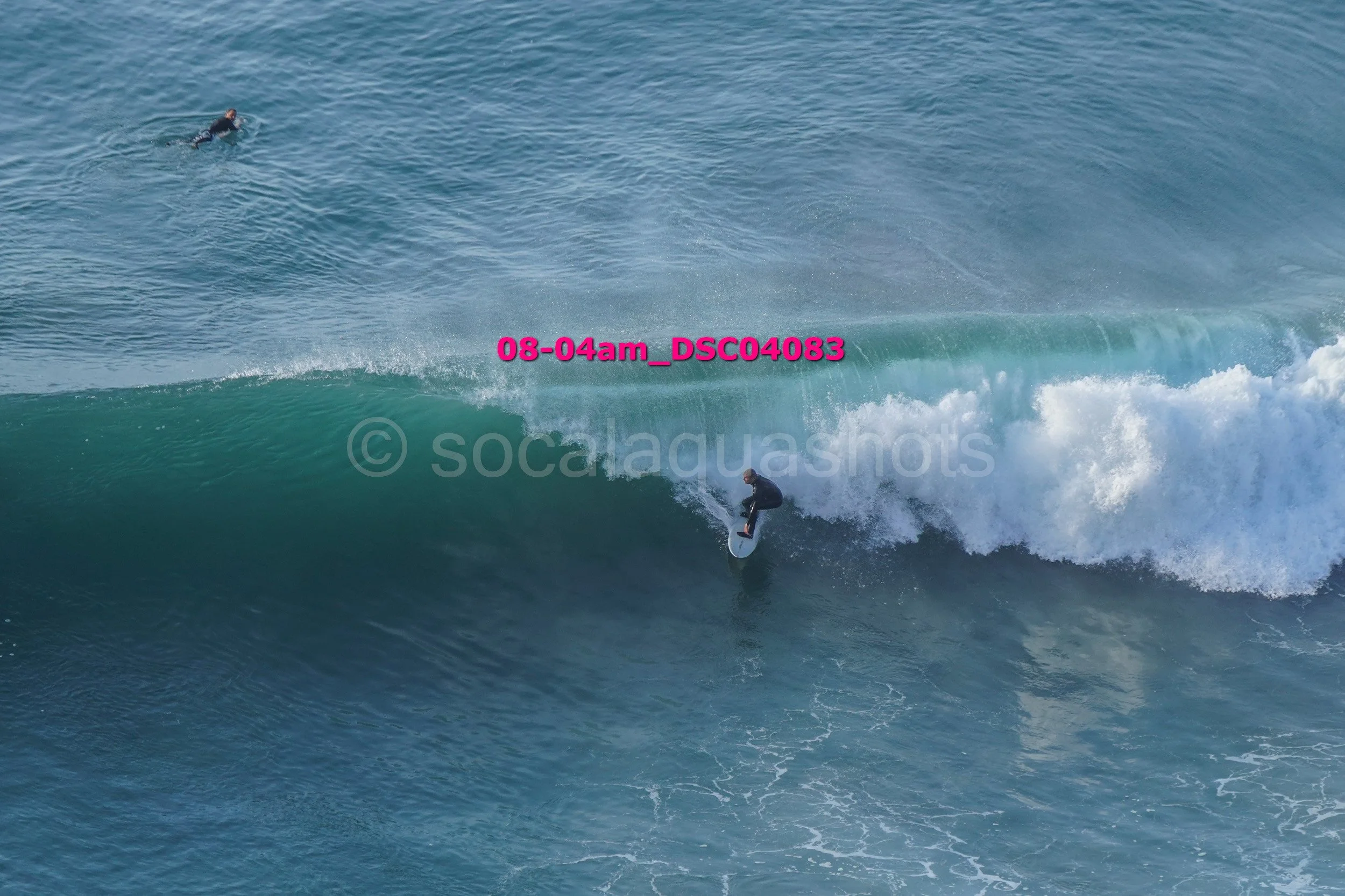 A person surfing a large wave in the ocean, with another person swimming nearby.