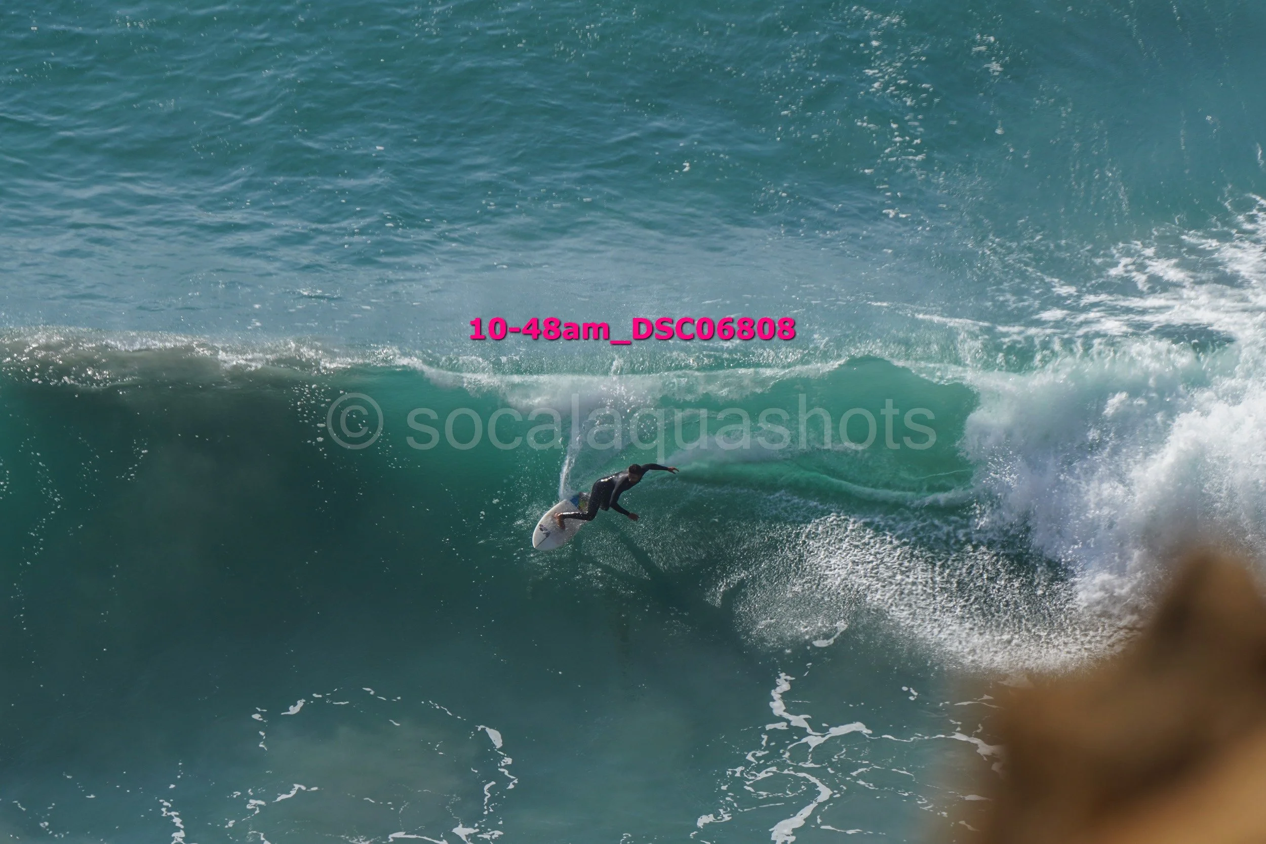 A surfer riding a large wave in the ocean, with the text '10-48am_DSC06808' in pink overlaying the water.
