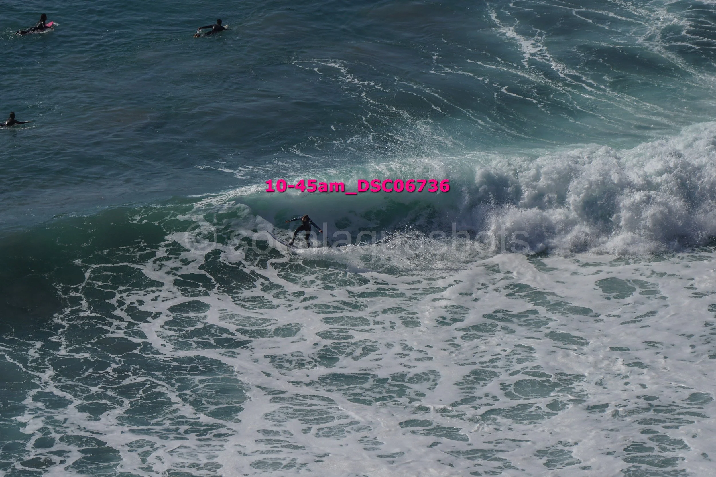 A person surfing on a wave in the ocean, with other surfers in the background.