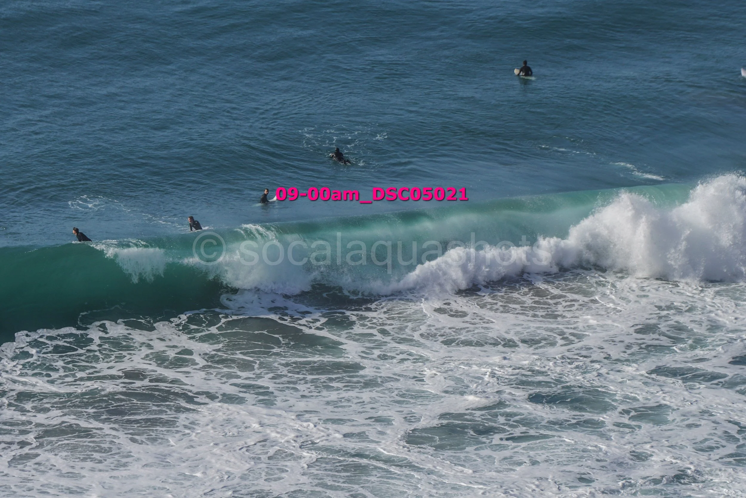 Surfers in wetsuits riding and sitting on waves in the ocean.