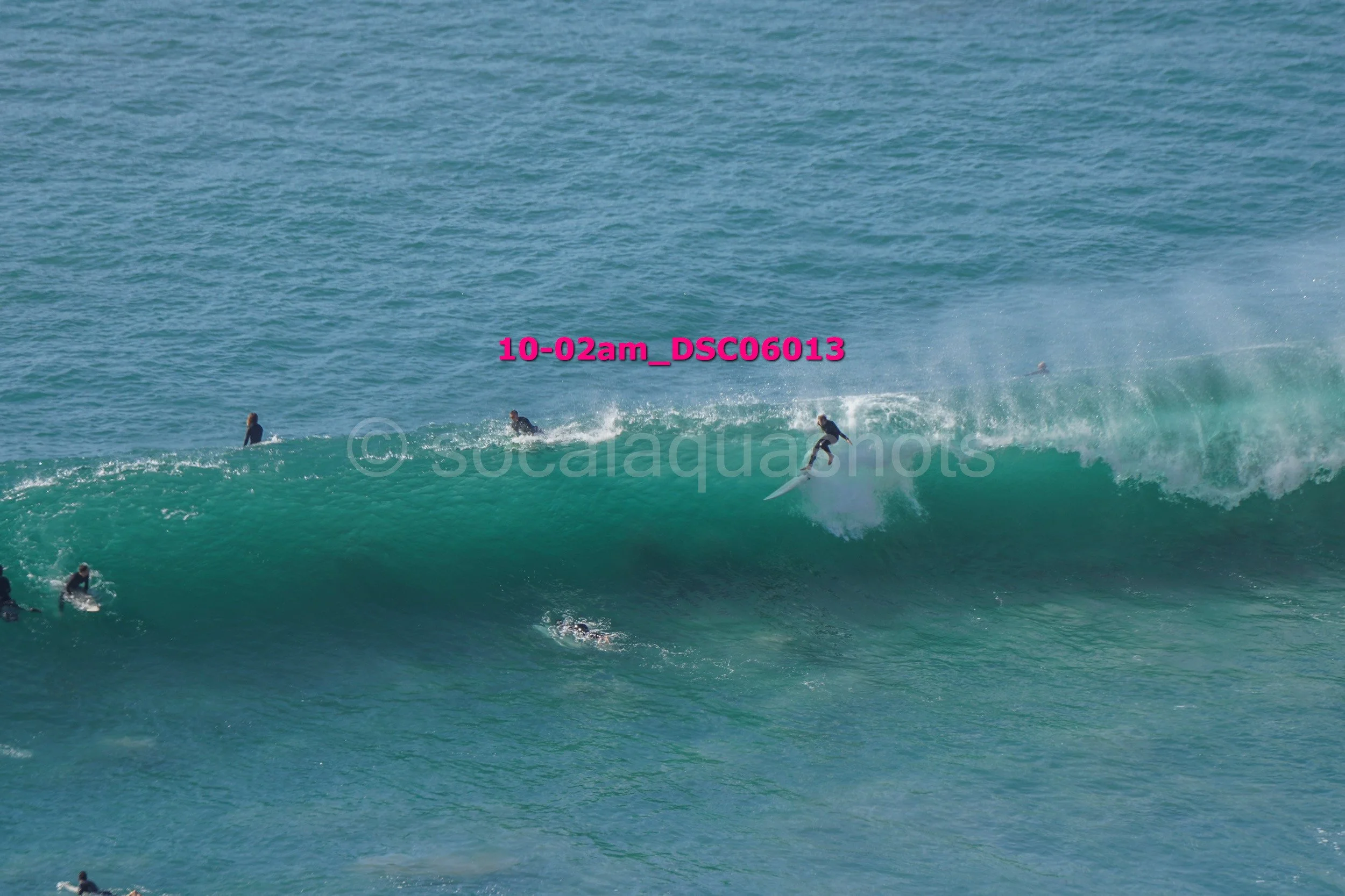 Surfer riding a large wave with others in the water and a few standing on the ocean in the background.