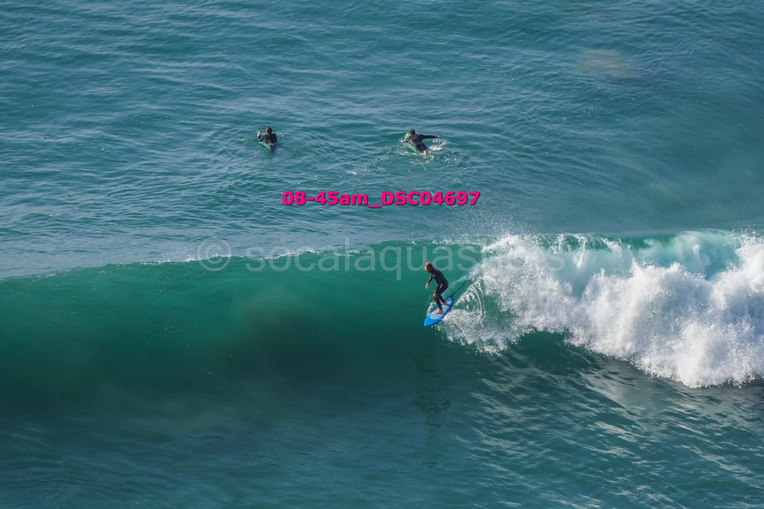 Person surfing on a large ocean wave with two other surfers in the background