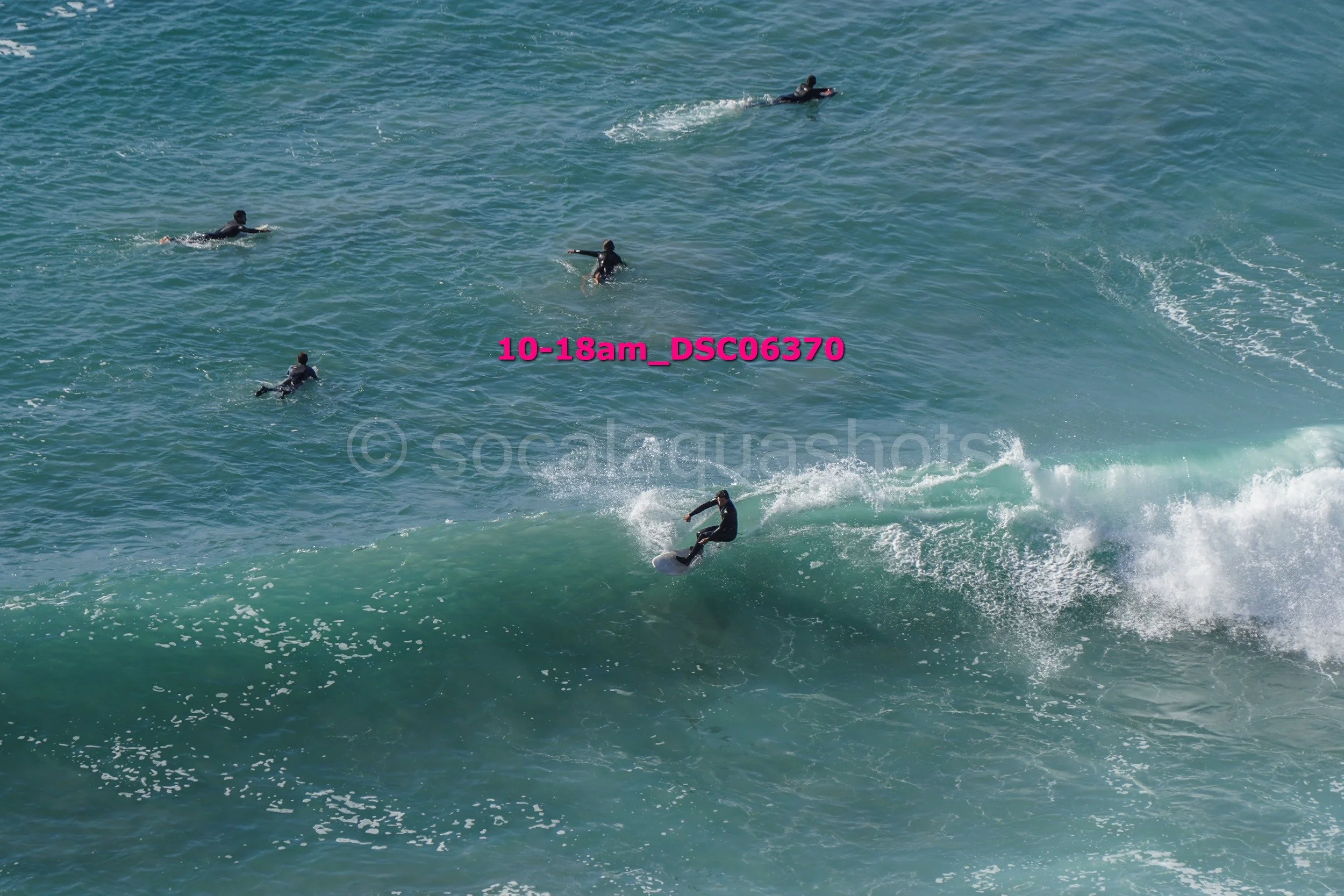 Surfer riding a wave while five others are swimming or paddling in the ocean.