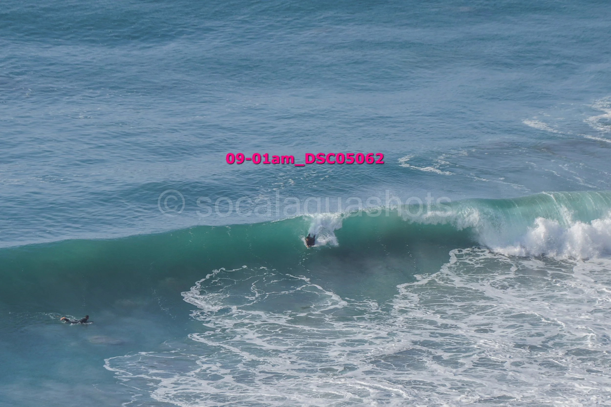 A surfer riding a large wave in the ocean, with another surfer swimming in the water.