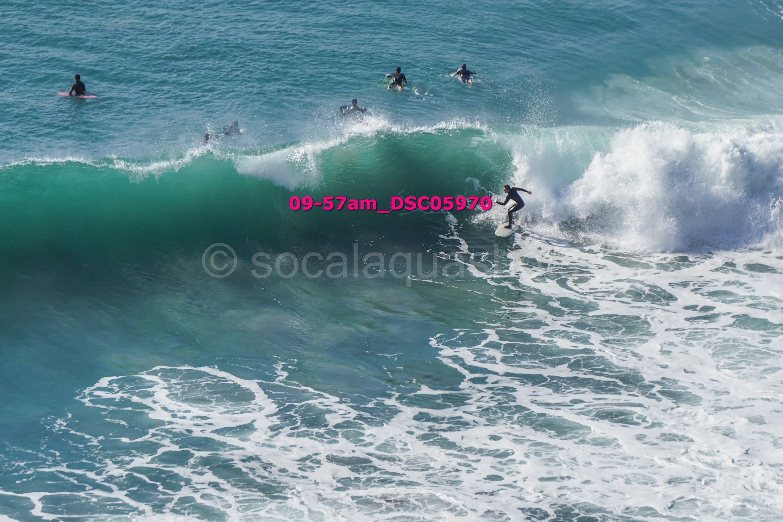 A surfer riding a wave with several other surfers in the water nearby.