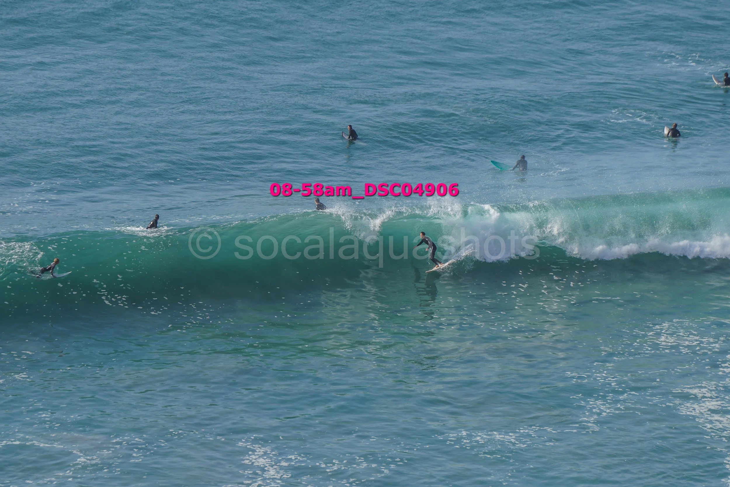 People surfing on waves in the ocean, some on surfboards and some on paddleboards, with water spray in the background.